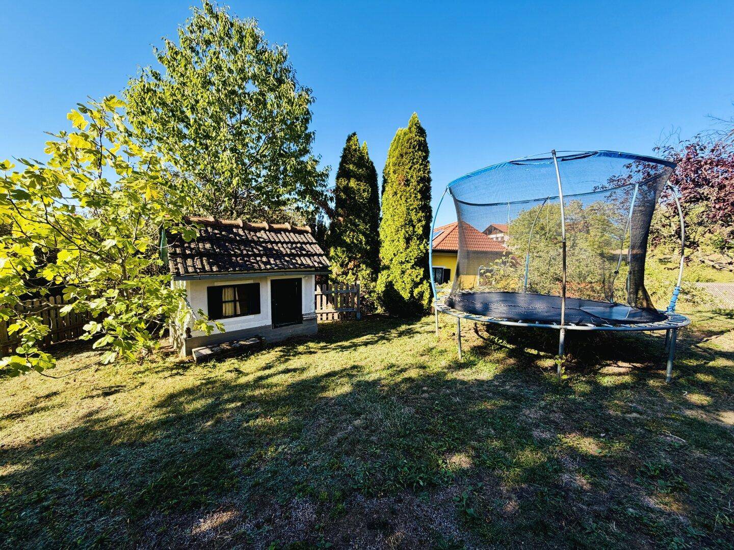 Sonniger Gartenbereich mit großem Trampolin und charmantem Spielhaus für Kinder.