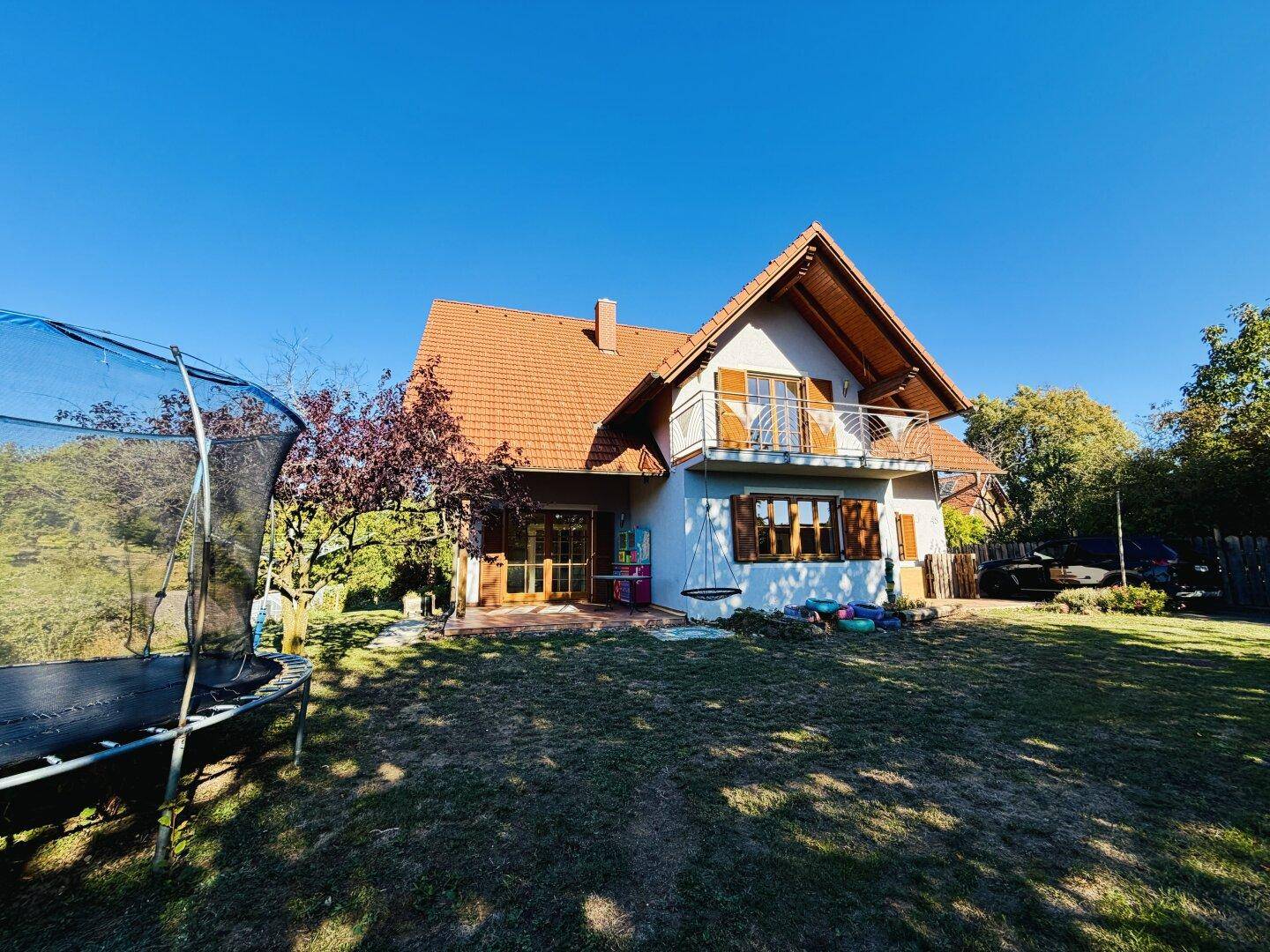 Hinteransicht des Hauses mit großem Garten, Trampolin und kleinem Balkon im Obergeschoss.