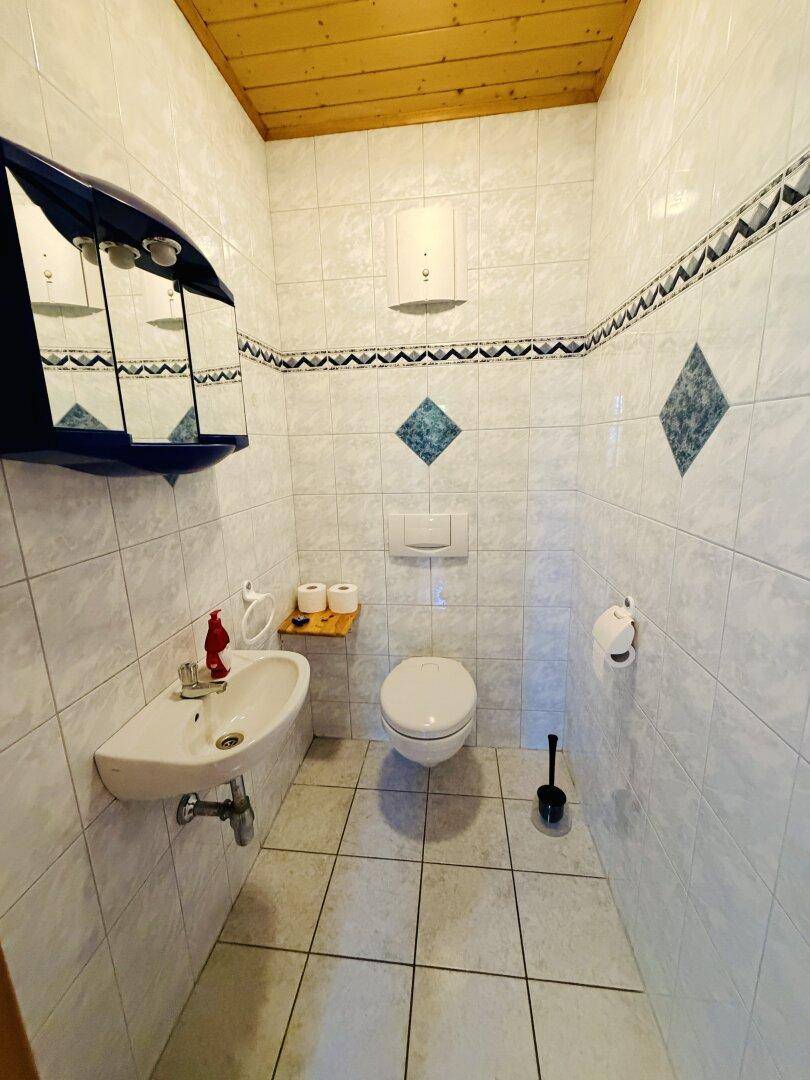 Kleines Gäste-WC mit weißen Fliesen, Holzdecke und einem wandhängenden WC.