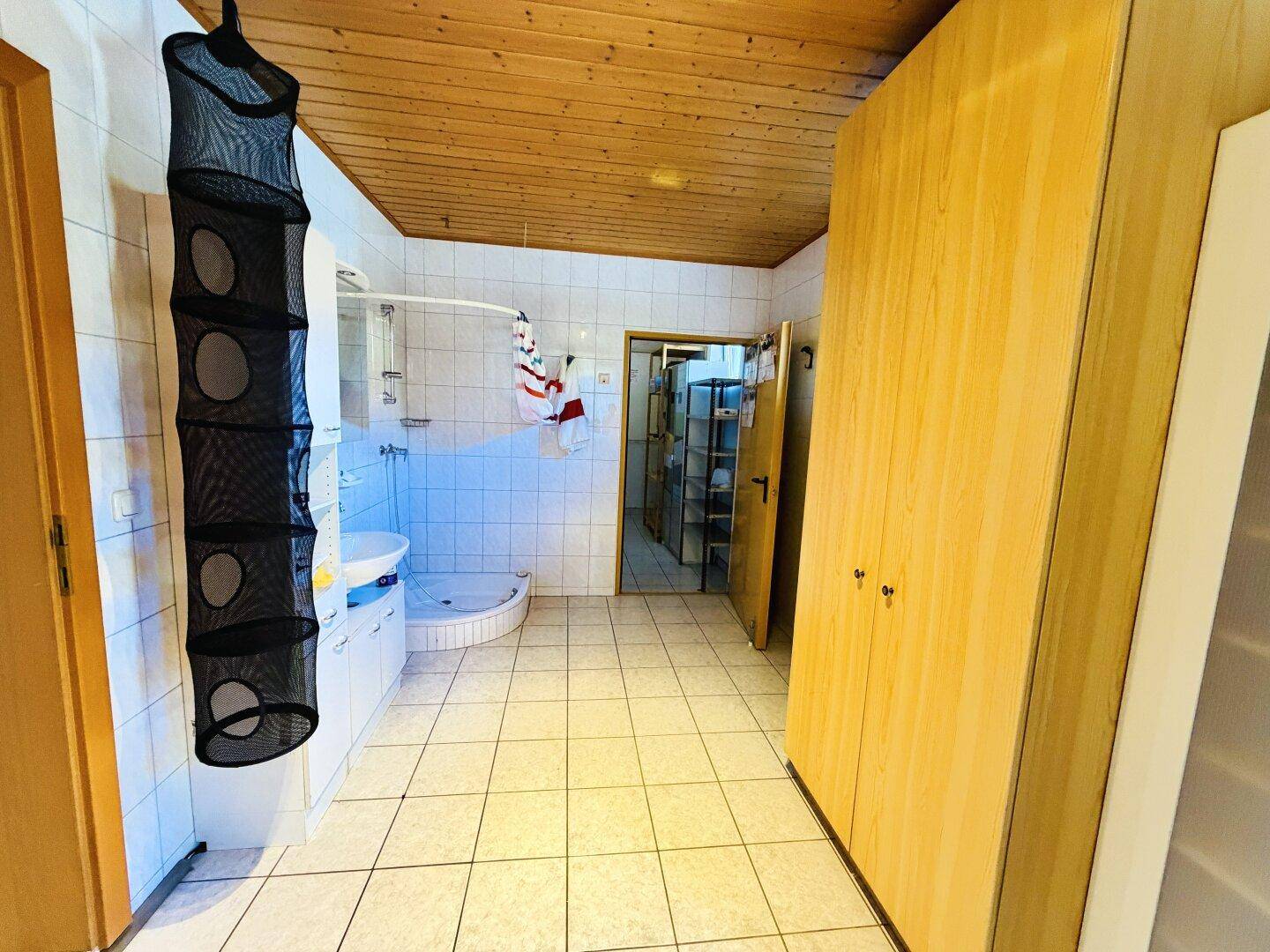 Badezimmer mit Duschkabine, Fliesenboden und Holzdecke, sowie praktischen Einbauschränken.