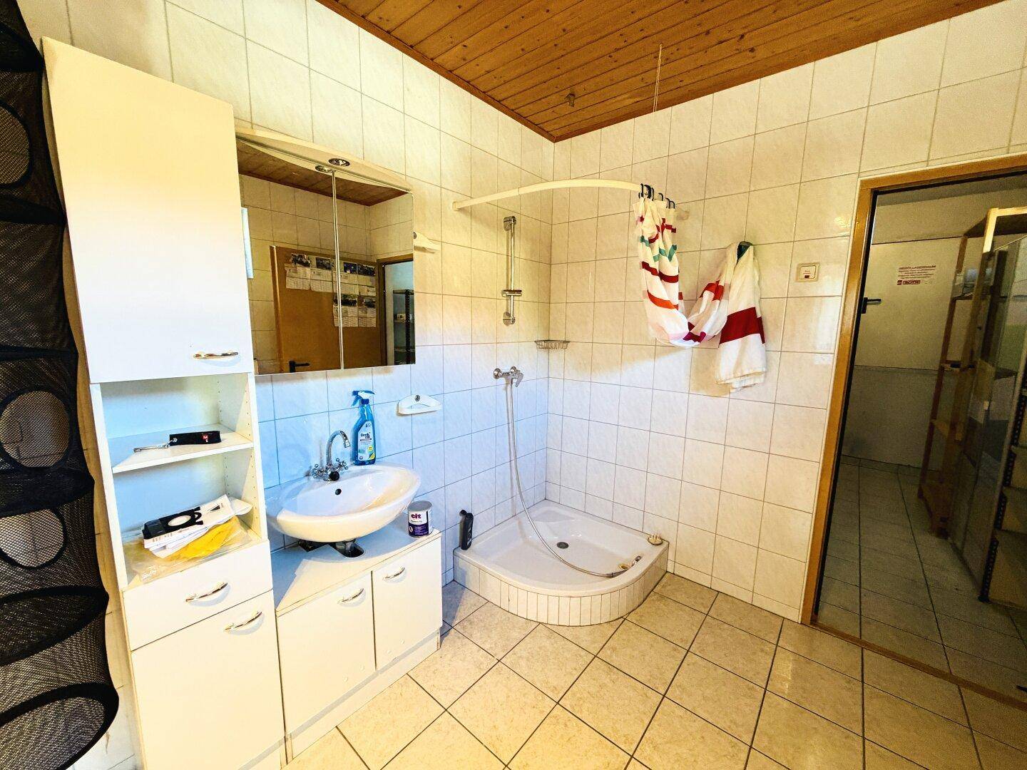 Helles Badezimmer mit Eckdusche, Waschbecken und Spiegelschrank, alles in hellen Fliesen gehalten.