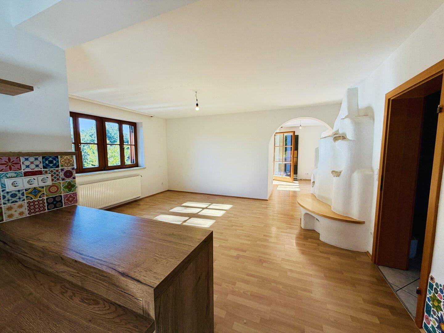 Offener Übergang von der Küche zum Wohnzimmer mit Holzboden und einem traditionellen Kachelofen.