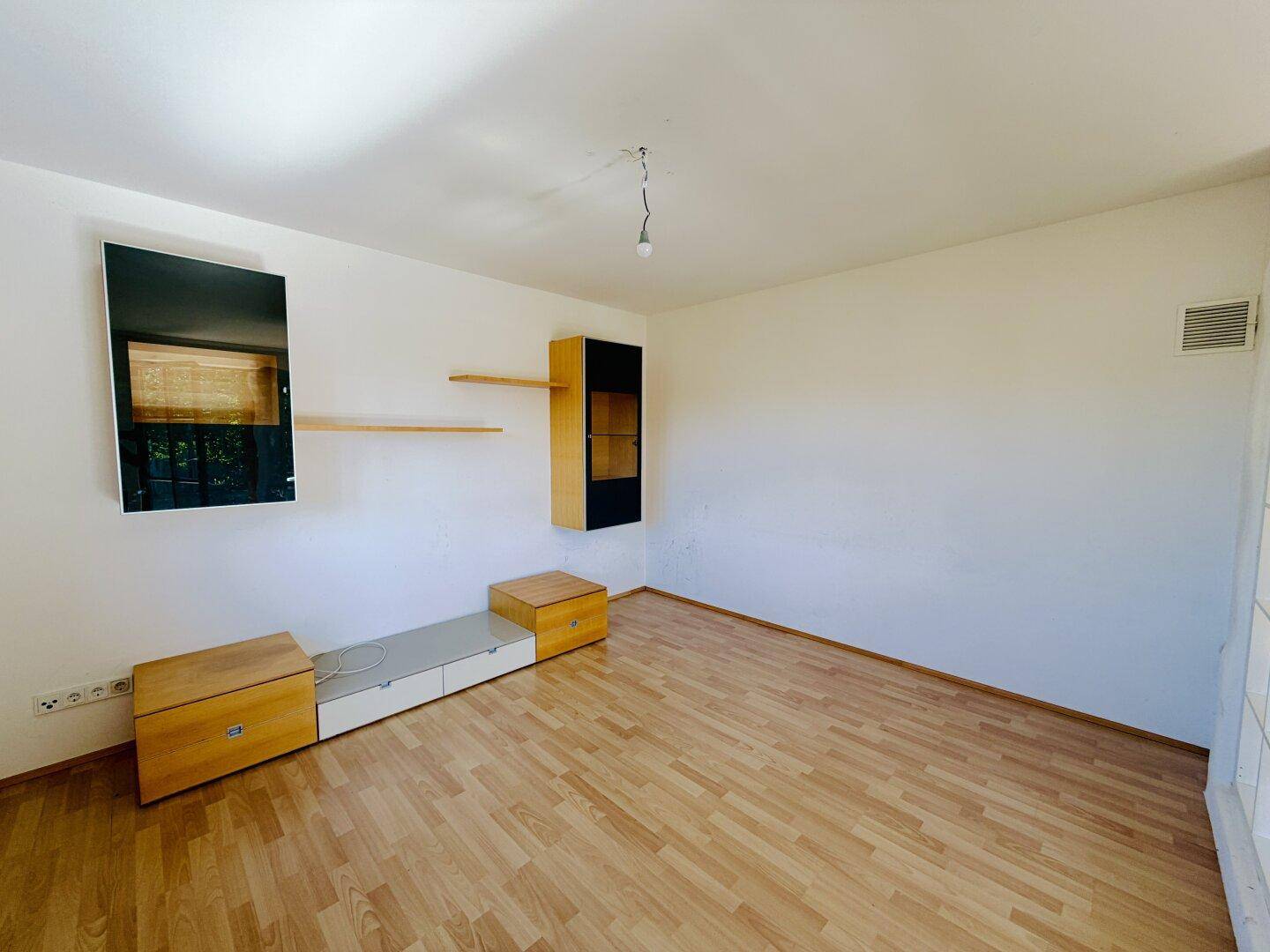 Heller Wohnbereich mit Laminatboden und schlichten Wänden, bietet viel Potenzial für persönliche Einrichtung.