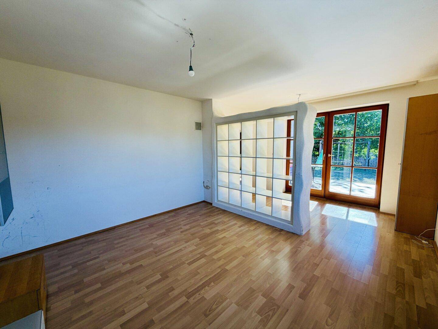 Wohnraum mit Laminatboden, einer Glasbausteinwand und einer großen Glastür, die ins Freie führt.