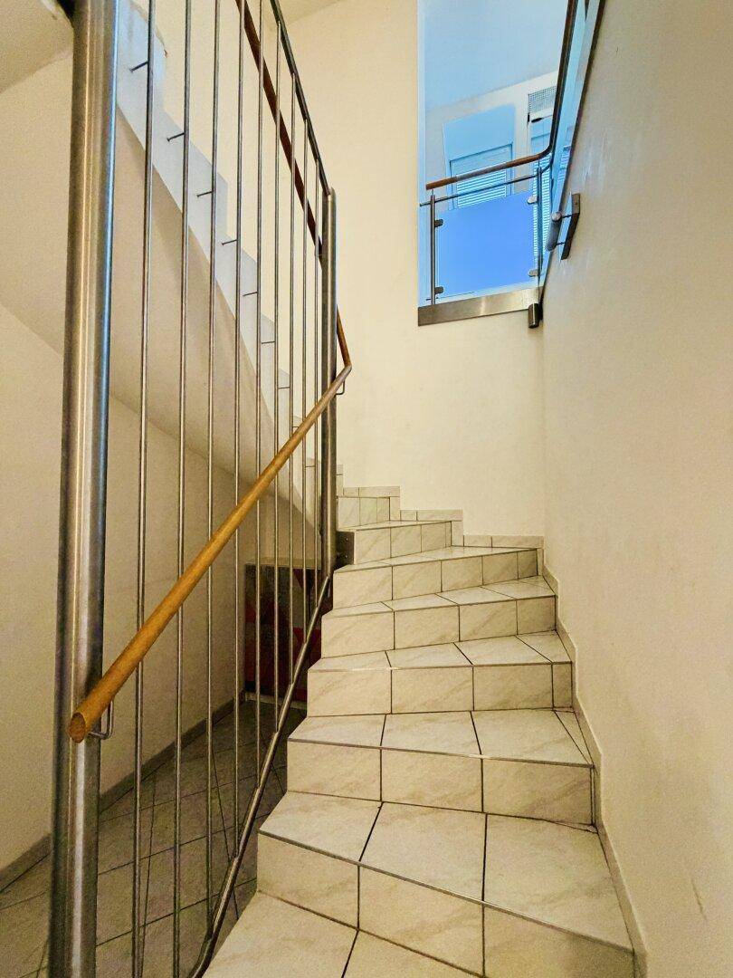 Modern geflieste Treppe mit Edelstahlgeländer und Holzhandlauf, die zu den oberen Etagen führt.