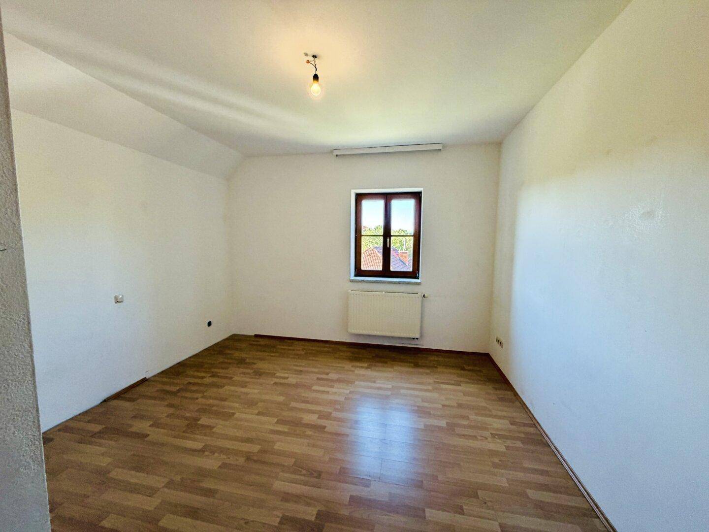 Geräumiges Schlafzimmer mit Laminatboden und einem Fenster, das viel natürliches Licht hereinlässt.