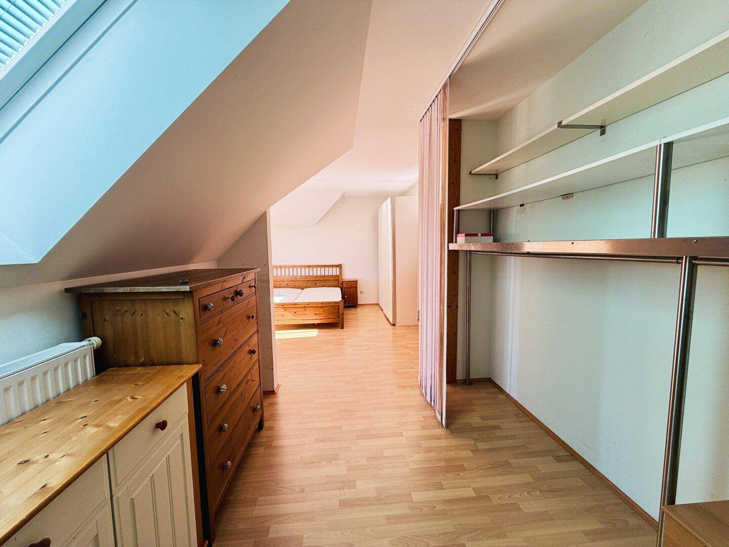 Begehbarer Kleiderschrank mit Kommode und Blick in das angrenzende Schlafzimmer mit Dachfenster.