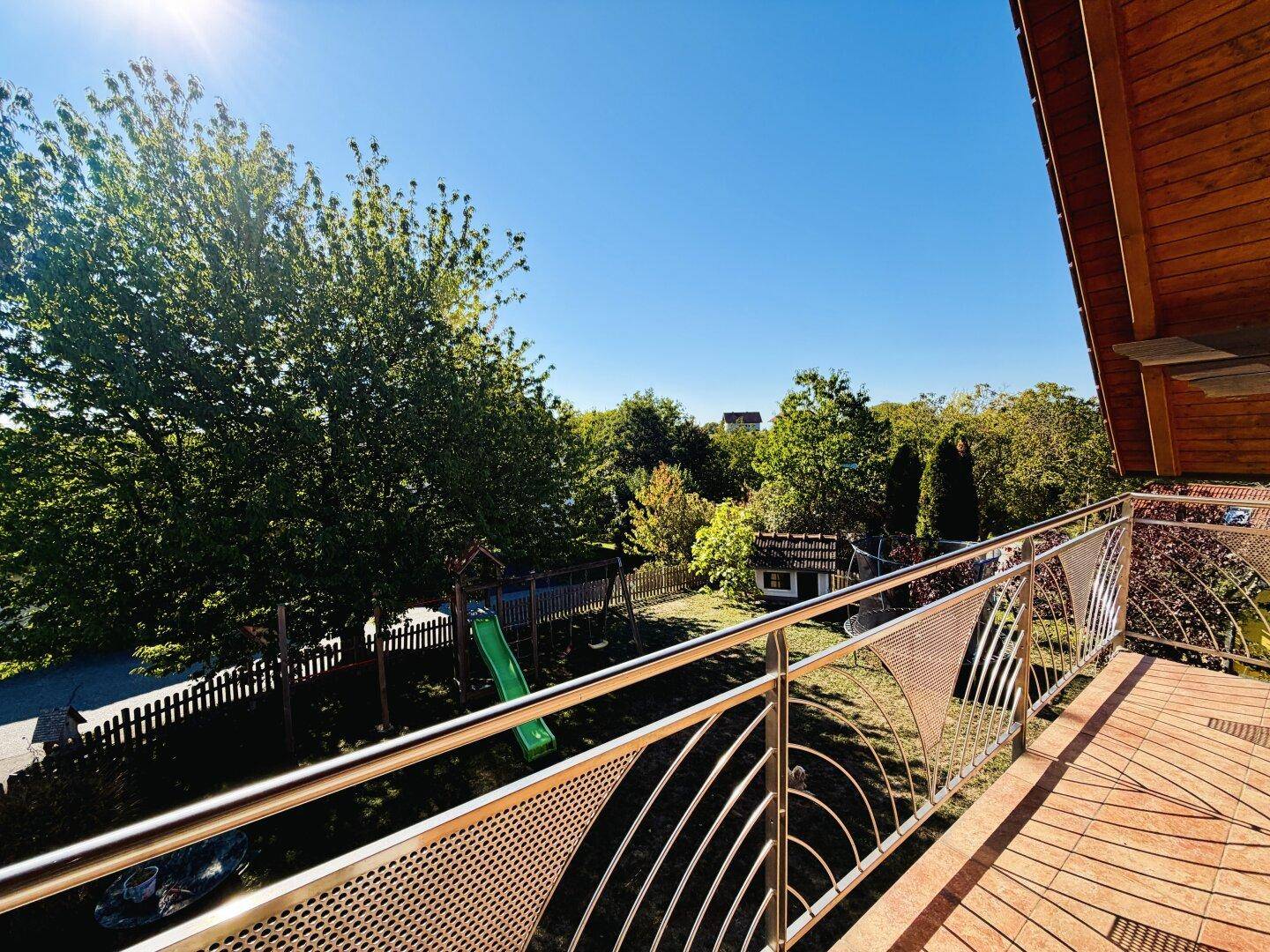 Sonniger Balkon mit Blick auf den Garten und einen Spielplatz, ideal für Familien.