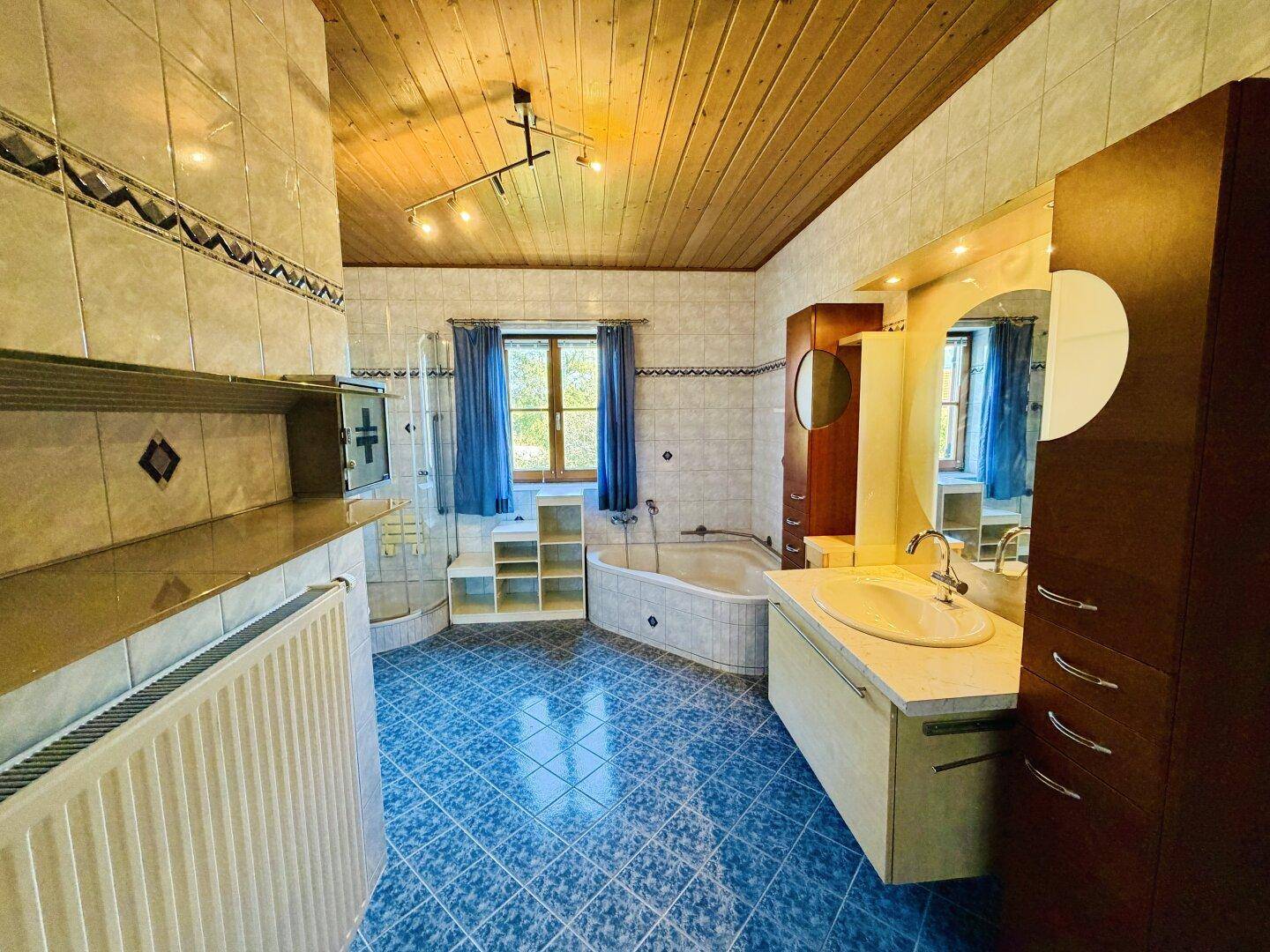 Geräumiges Badezimmer mit blauen Fliesen, Badewanne, Doppelwaschbecken und Holzdecke.