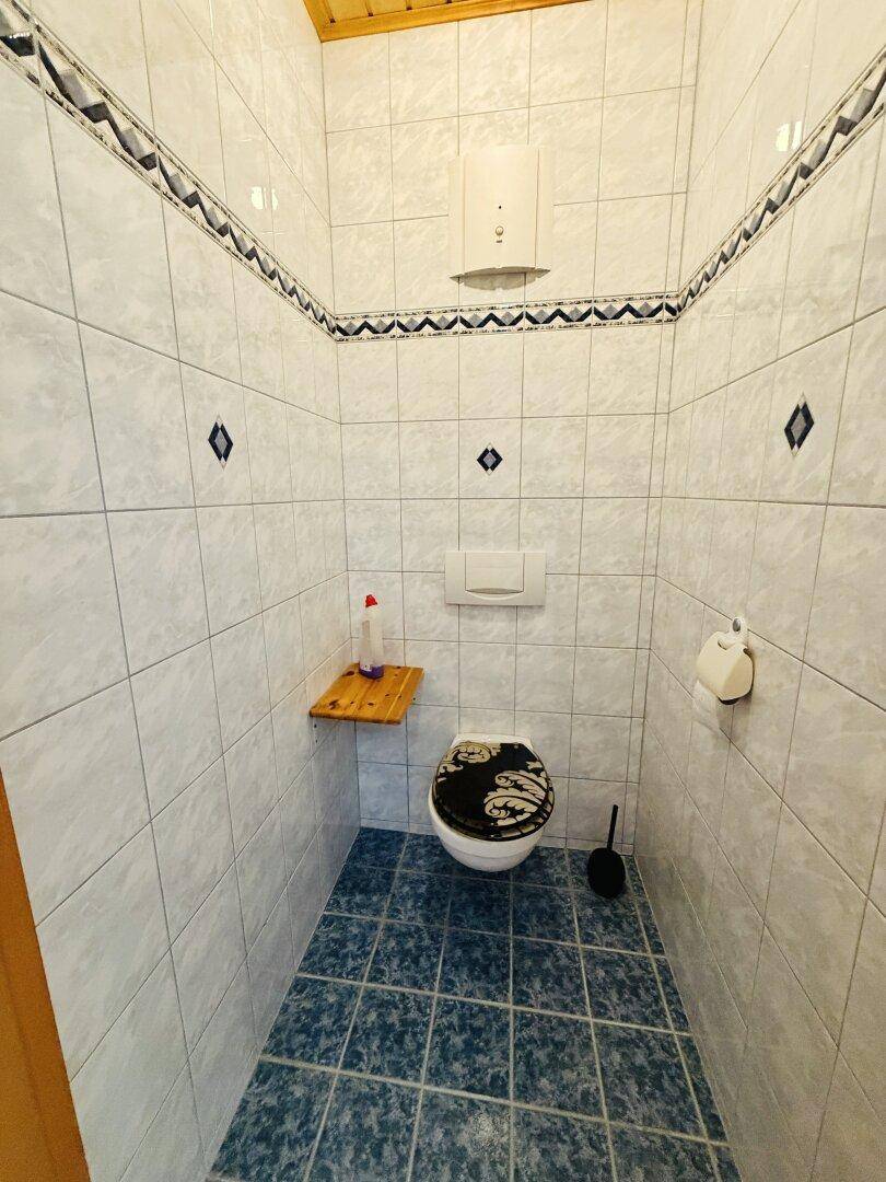 Kleines separates WC mit Wand-WC und Fliesenboden, ausgestattet mit einem Warmwasserbereiter.