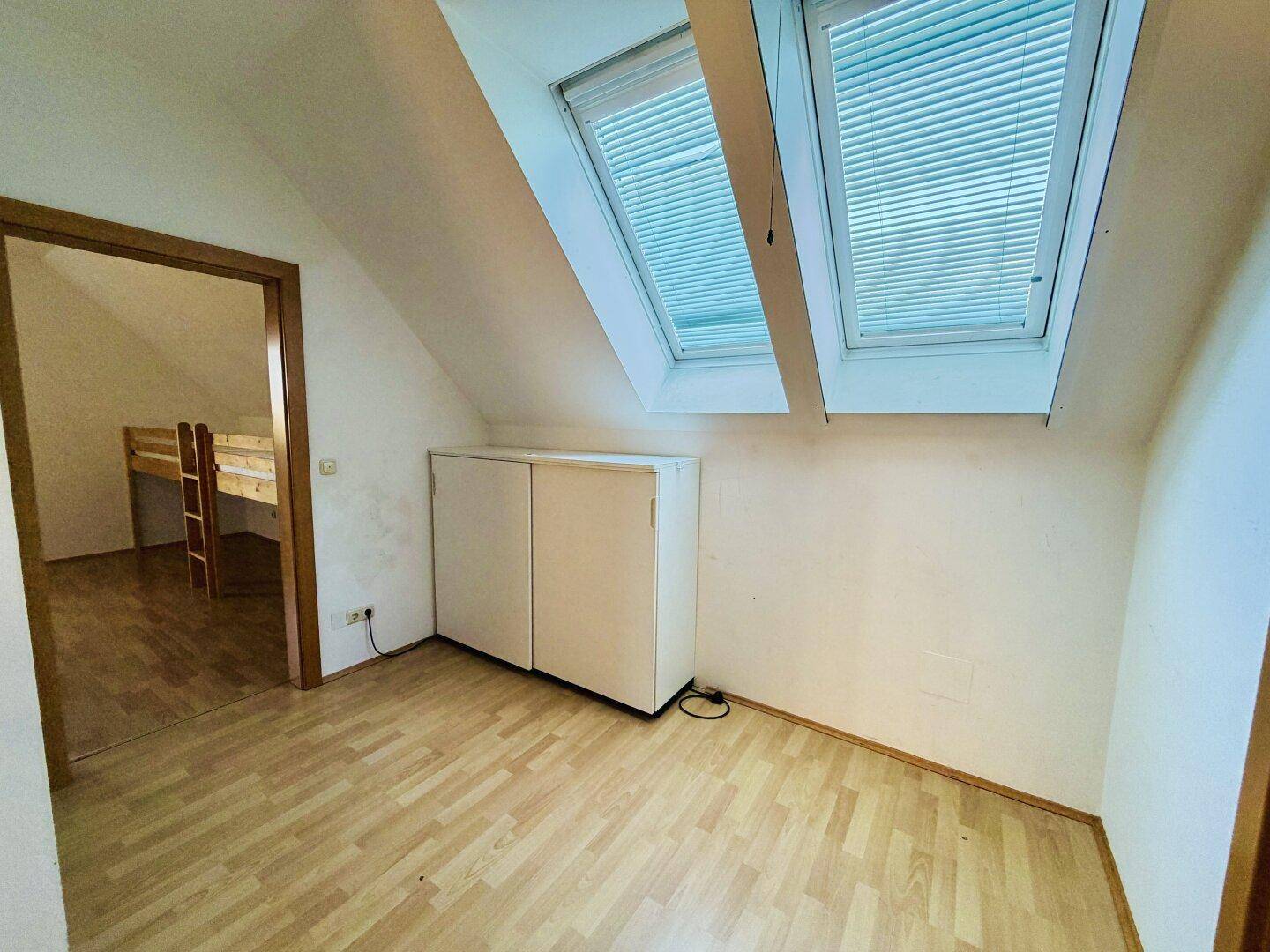 Dachzimmer mit zwei Dachfenstern, Laminatboden und Stauraum, ideal als Kinder- oder Gästezimmer.