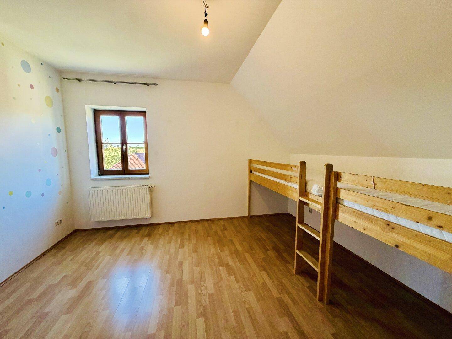 Helles Kinderzimmer im Dachgeschoss mit Etagenbett, Fenster und farbenfroher Wanddekoration.
