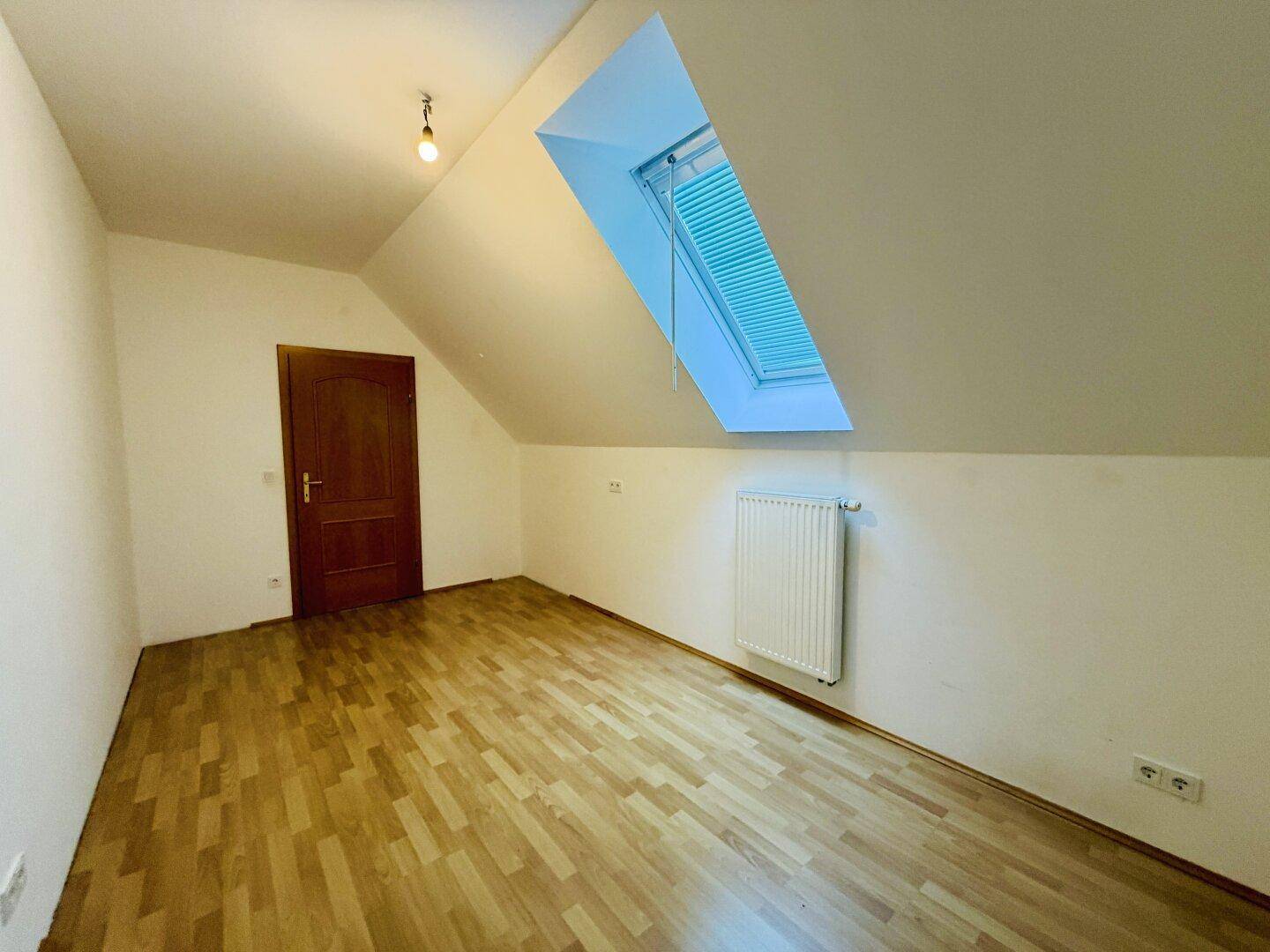 Dachzimmer mit Dachfenster, Laminatboden und Holztür, bietet viel natürliches Licht.