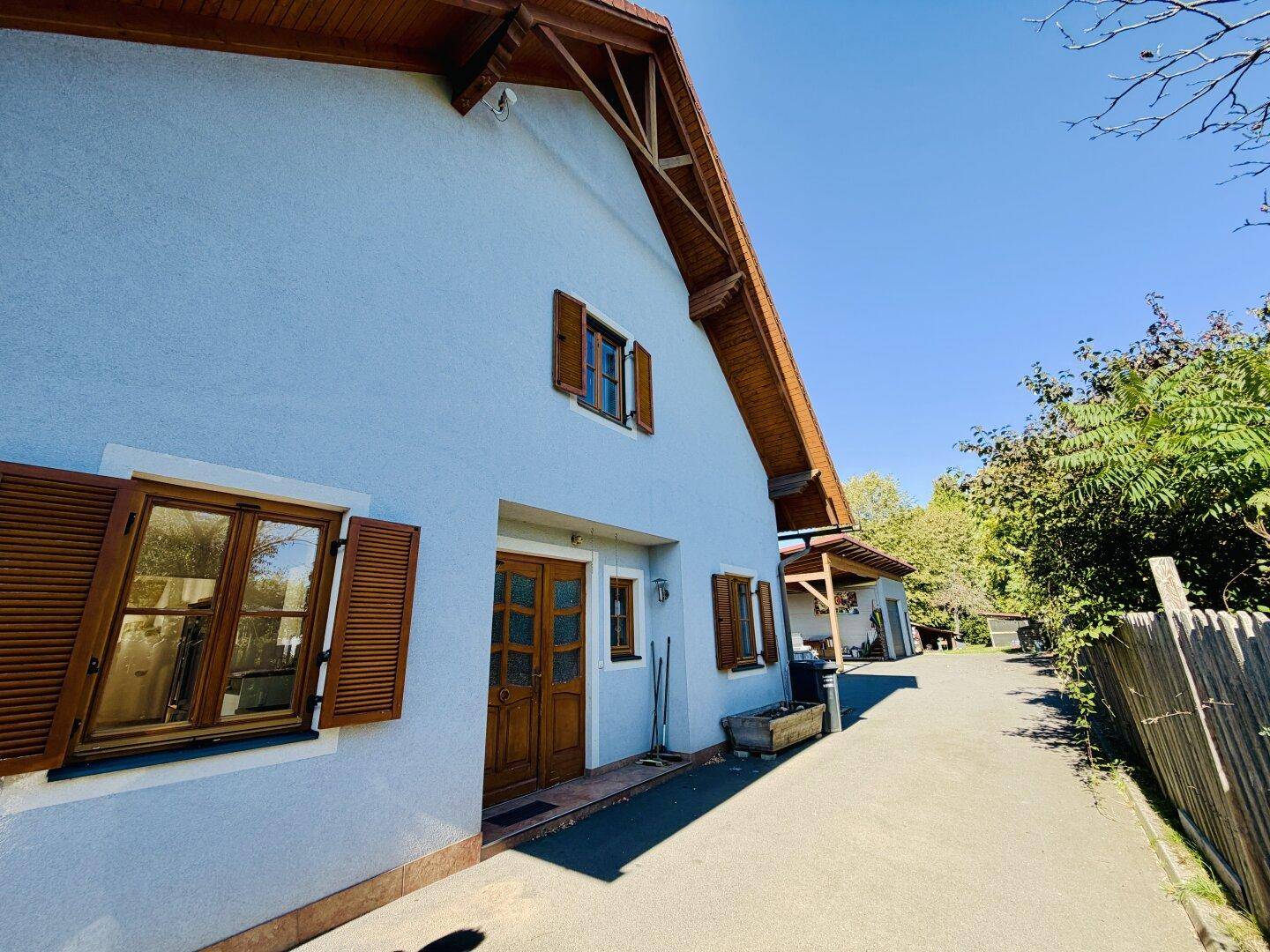 Vorderansicht eines Hauses mit hellblauer Fassade, Holzfenstern mit Fensterläden und Holztür.
