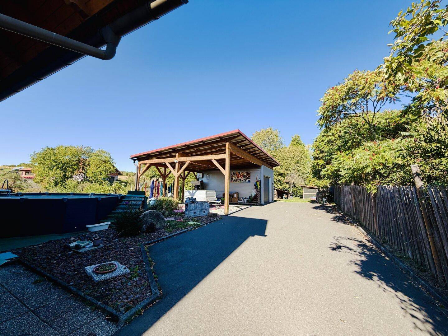 Zufahrt zum Grundstück mit Carport und Garage, umgeben von Bäumen und viel Grün.