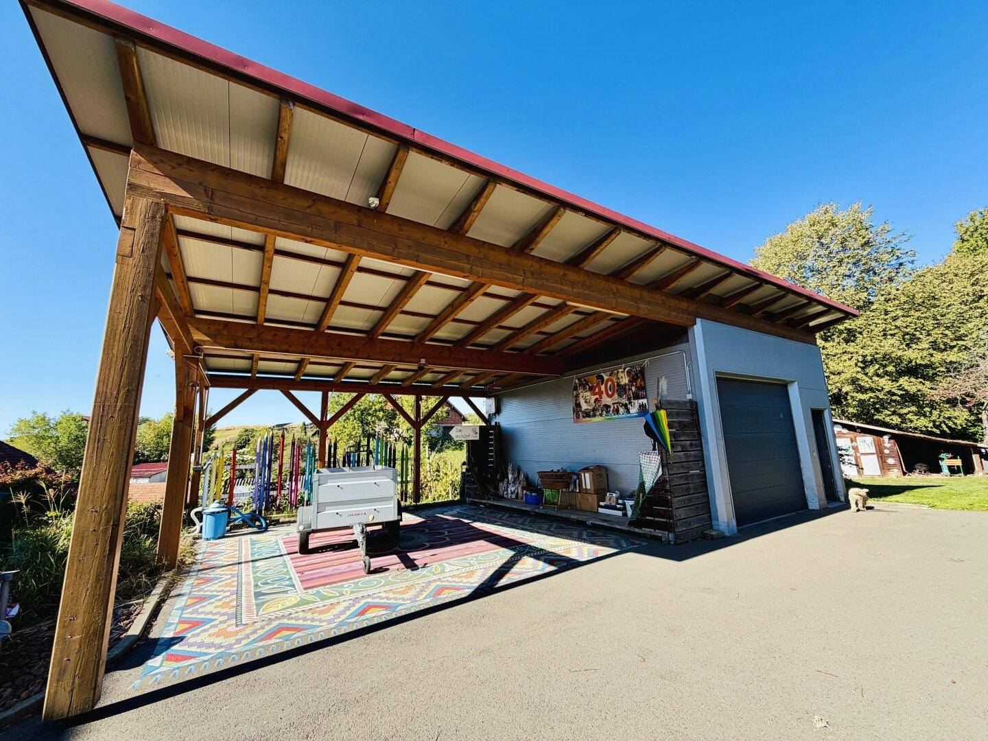 Geräumiger Carport mit Holzkonstruktion und angrenzender Garage, bietet Schutz für Fahrzeuge.