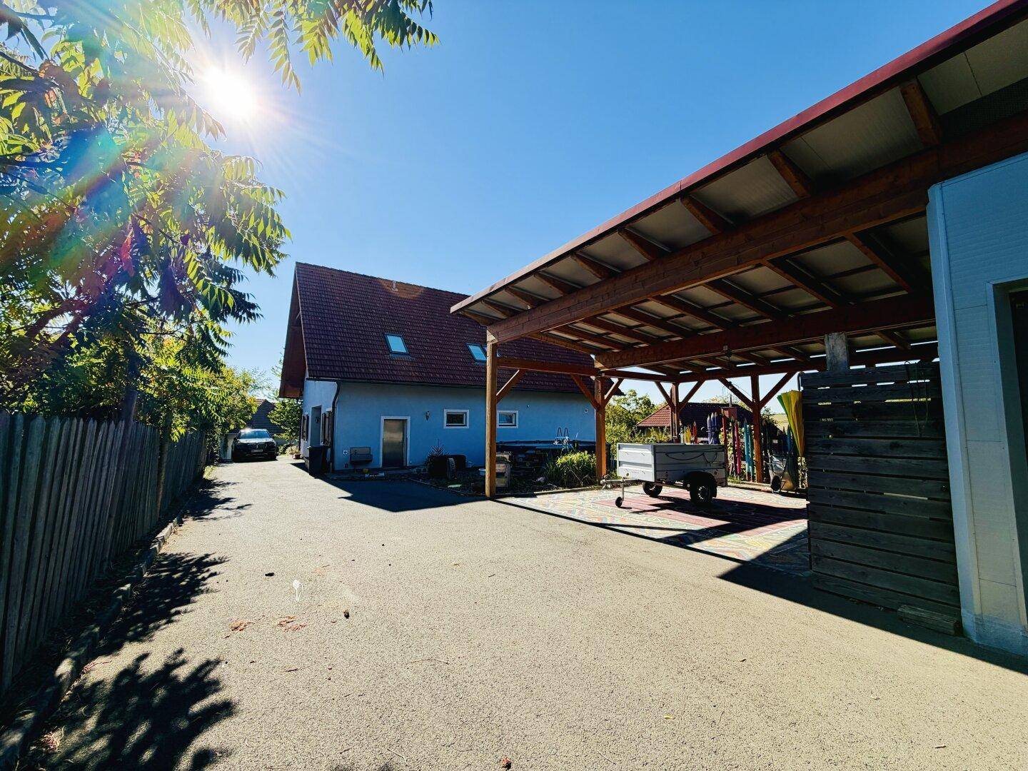 Sonniger Zufahrtsbereich zum Haus und Carport, umgeben von üppigem Grün.