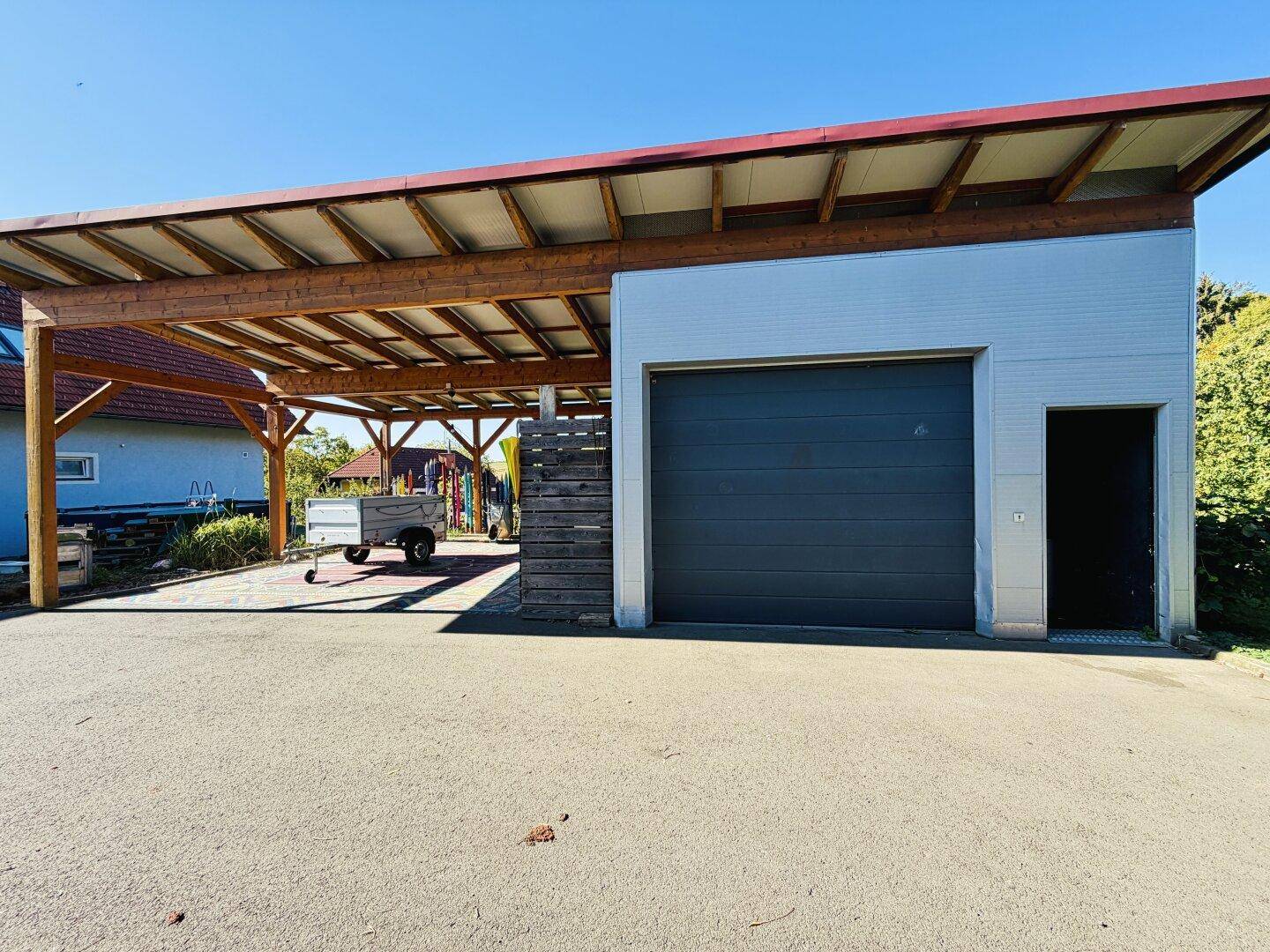 Carport mit Holzkonstruktion und angrenzender Garage mit geschlossenem dunklem Tor.