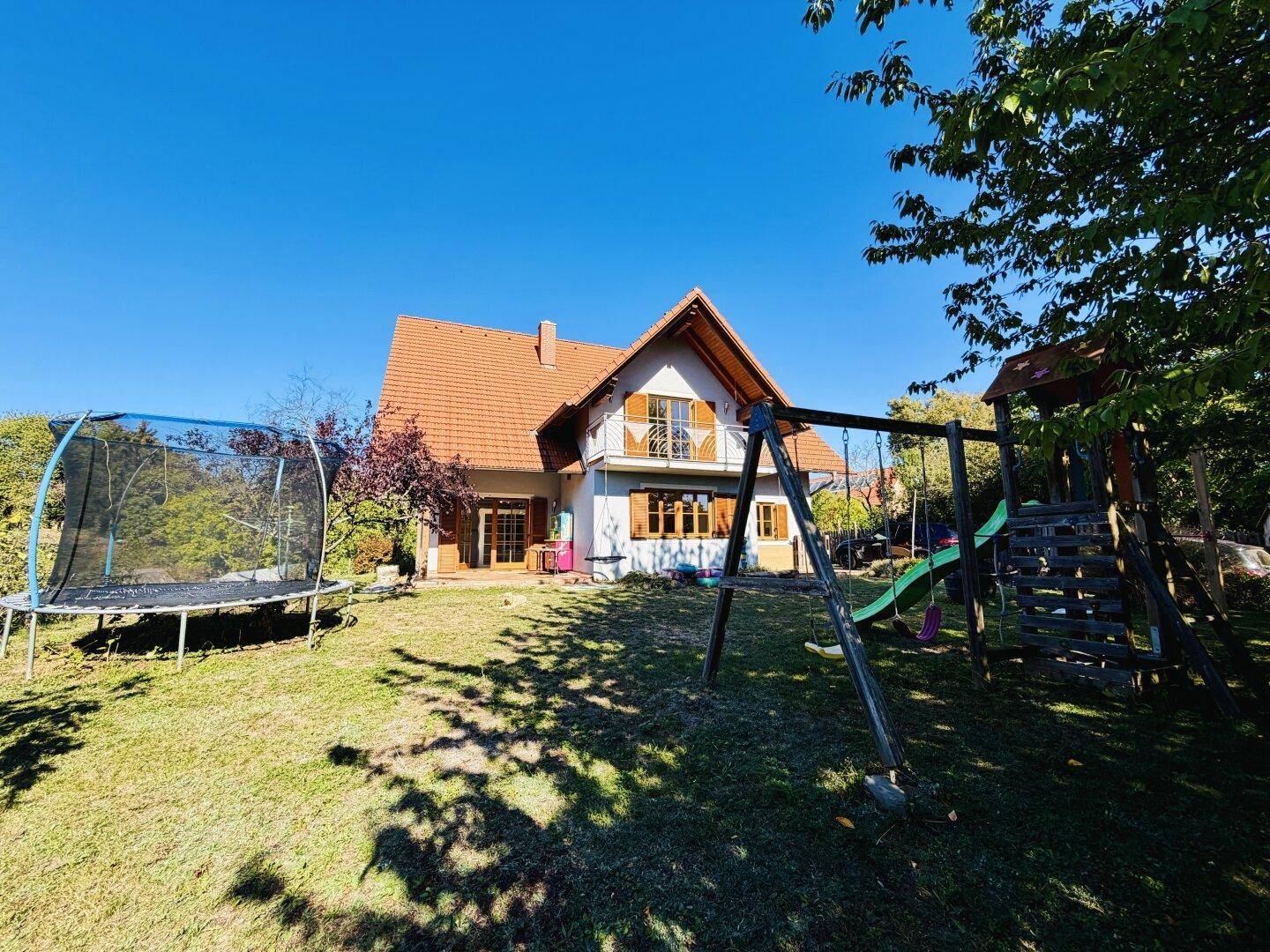 Weitläufiger Garten mit Spielplatz, Trampolin und Blick auf die Hausfassade mit Balkon.