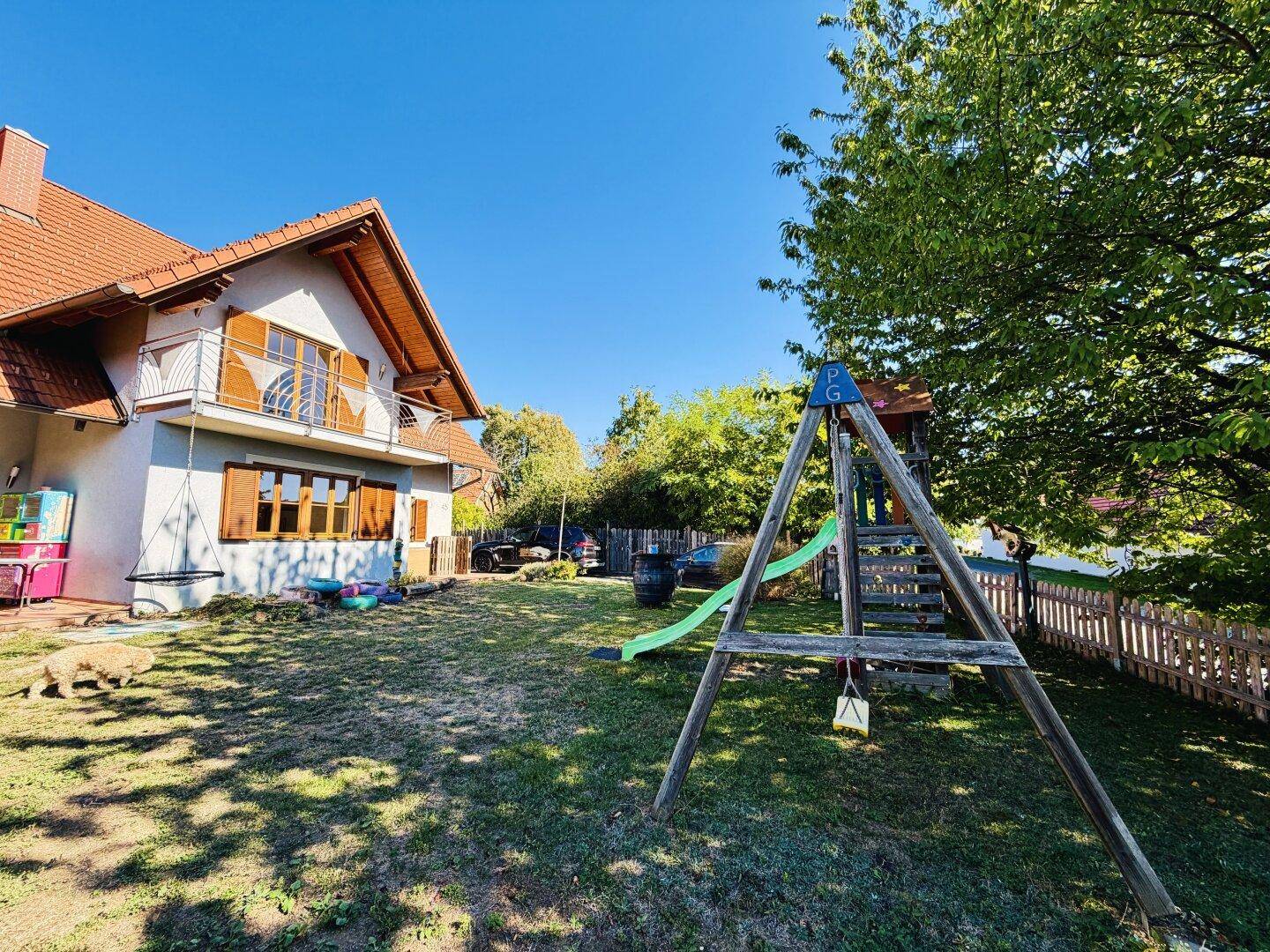 Seitlicher Gartenbereich mit Spielplatz und Blick auf die Hausfassade und den Zaun.