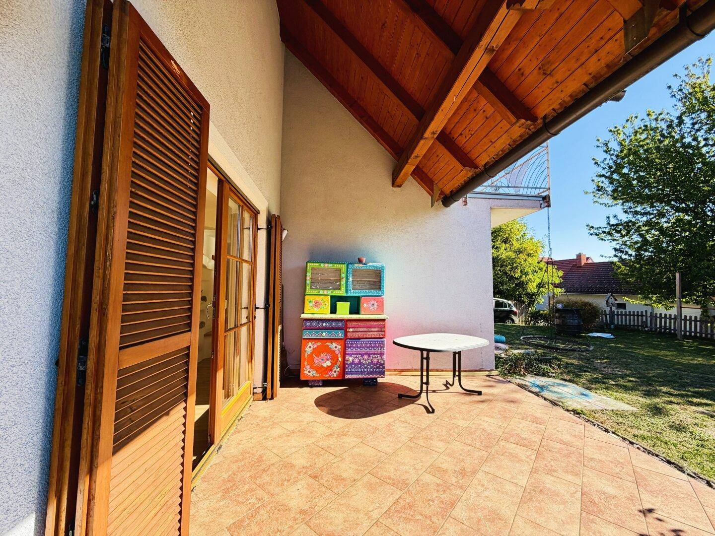 Detailansicht der gefliesten Terrasse mit kleinem Tisch und farbenfrohem Schrank unter Holzdach.