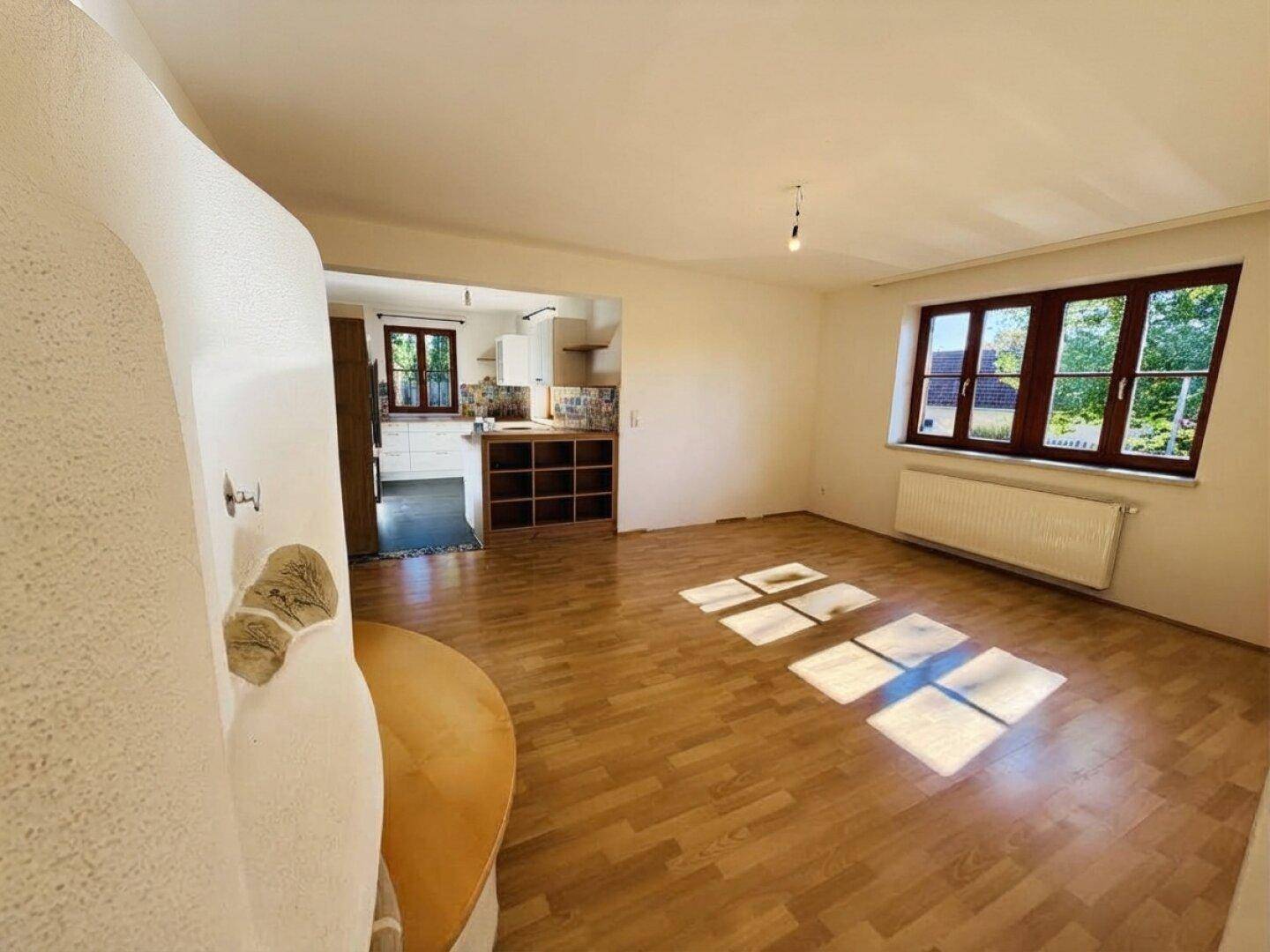 Offener Wohnbereich mit Laminatboden und viel Tageslicht, angrenzend an eine helle Küche.