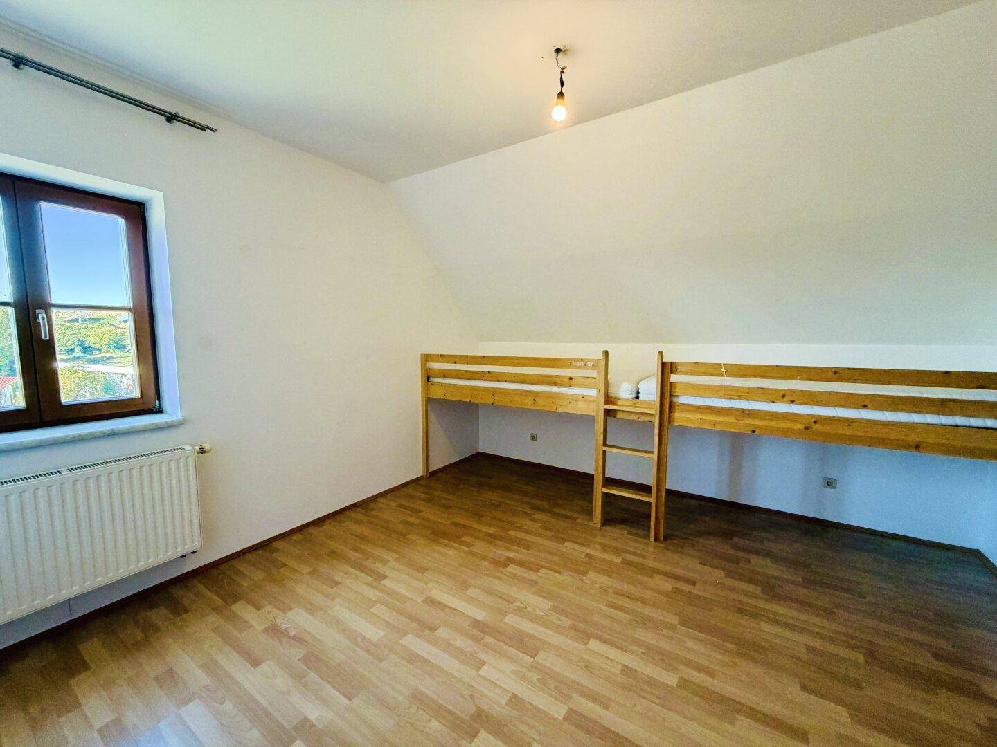 Geräumiges Schlafzimmer im Dachgeschoss mit Etagenbett, Fenster und Laminatboden, gut beleuchtet.