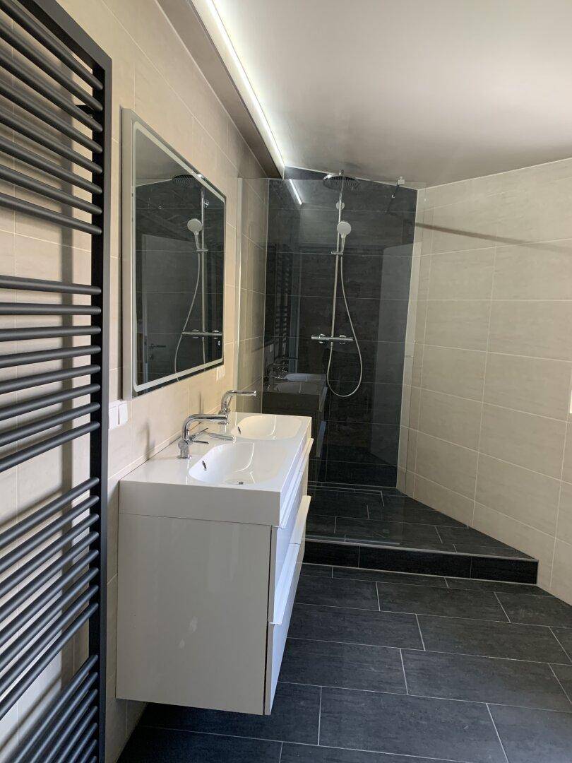 Helles Badezimmer mit modernen Fliesen, Doppelwaschbecken und geräumiger Duschkabine.