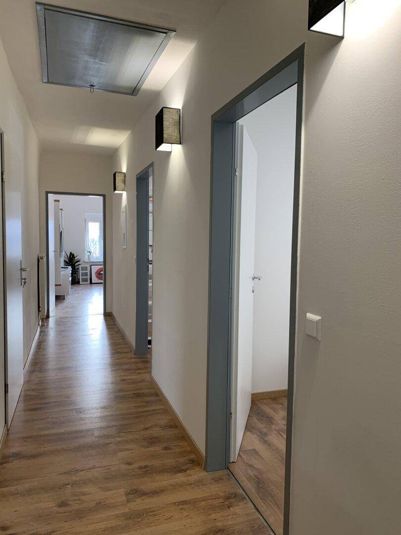 Heller Flur mit mehreren Türen, Holzboden und modernen Wandleuchten.