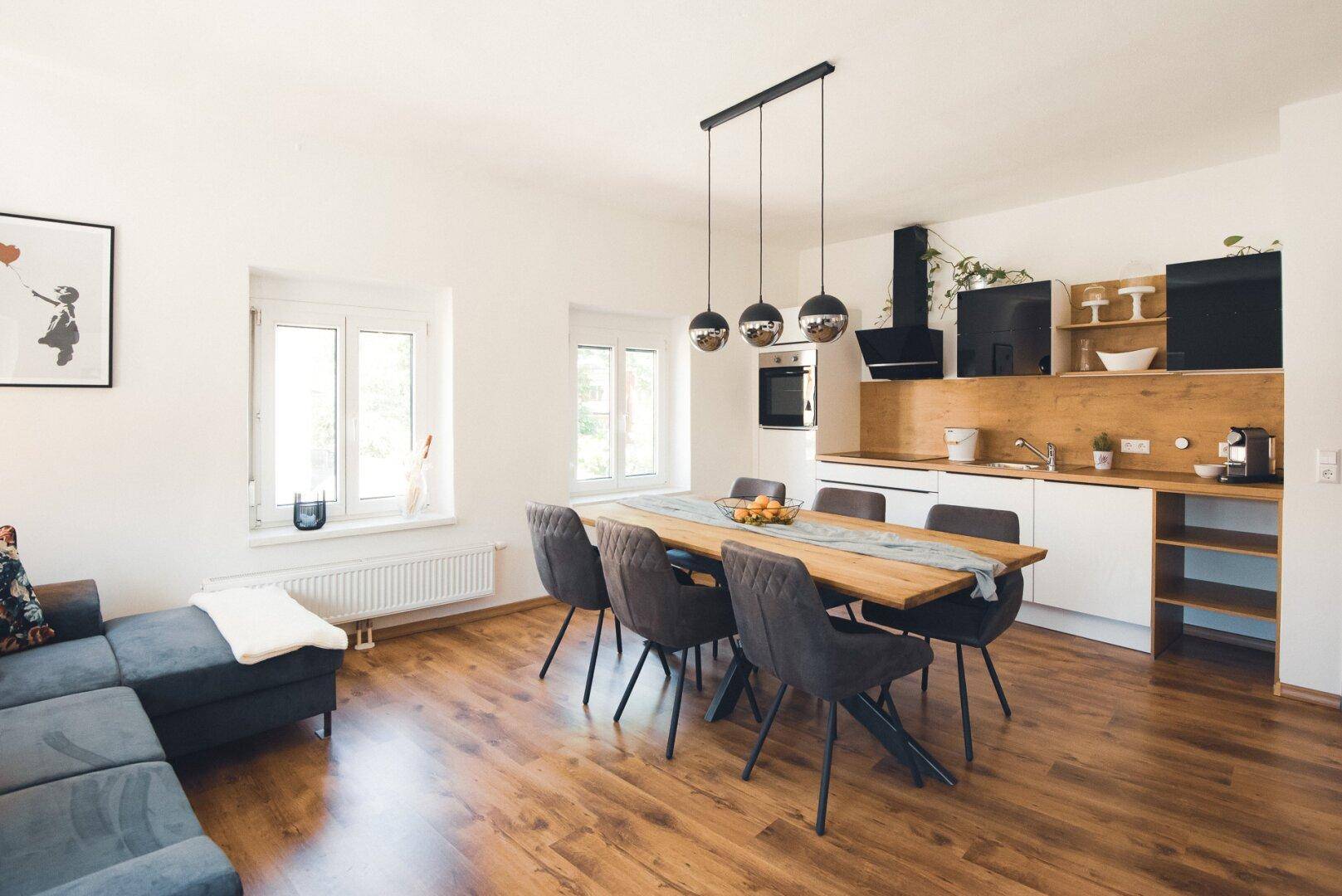 Geräumiger Wohnbereich mit offener Küche, Essbereich und Sofa, alles auf Holzboden.