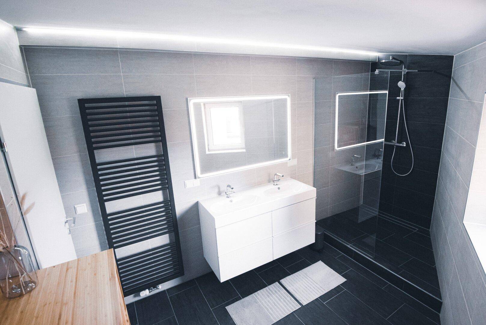 Modernes Badezimmer mit Doppelwaschbecken, großer Duschkabine und Handtuchheizkörper.