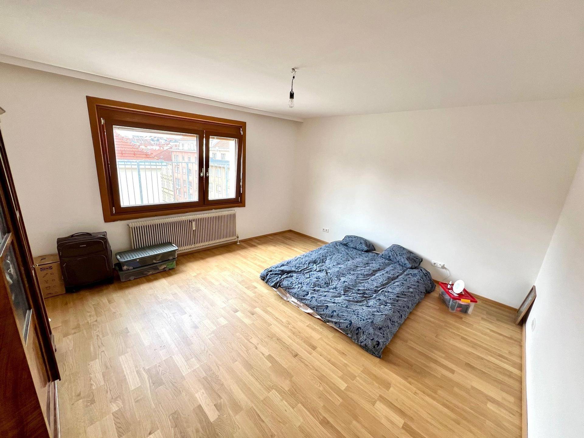 Schlafzimmer mit Parkettboden, Blick auf die Dächer und einfacher Einrichtung, die Ruhe ausstrahlt.