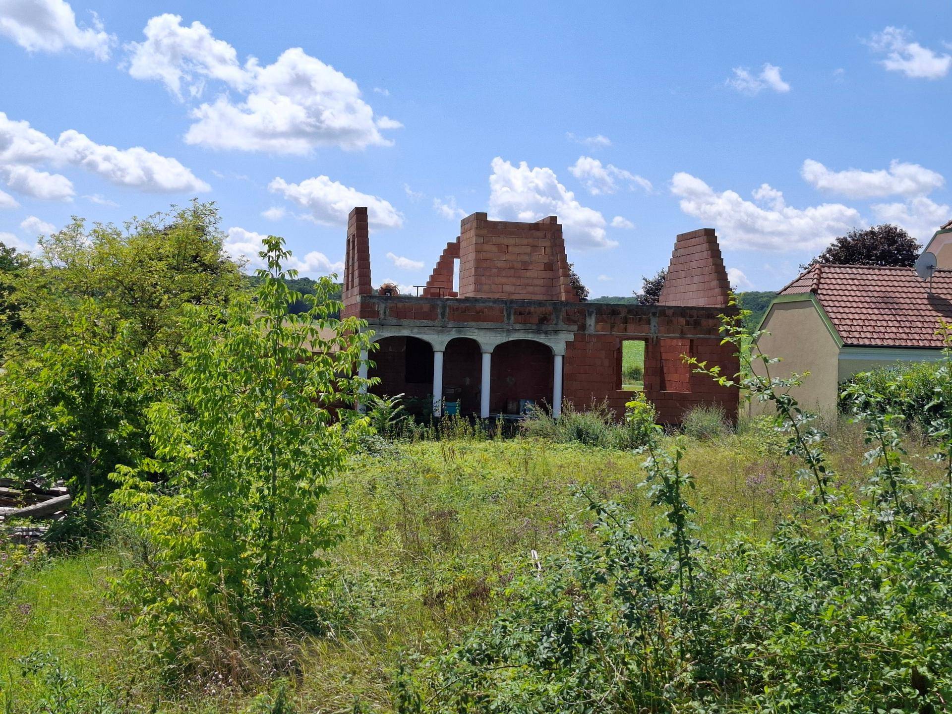 Distanziert aufgenommener Rohbau eines Hauses mit Säulenstruktur und umgebender Natur.