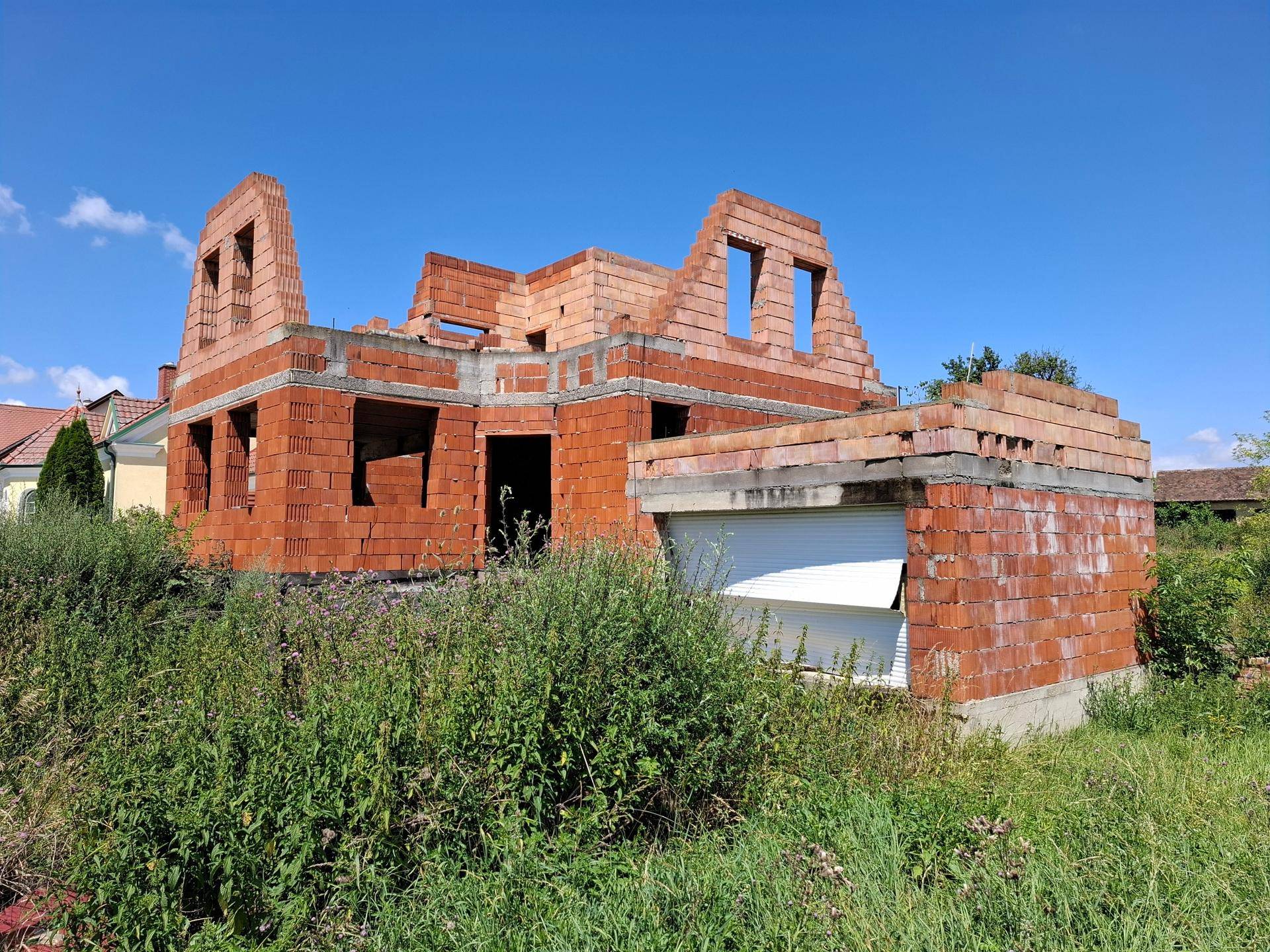 Rohbau eines Hauses mit Ziegelwänden und einer integrierten Garagenstruktur im Grünen.