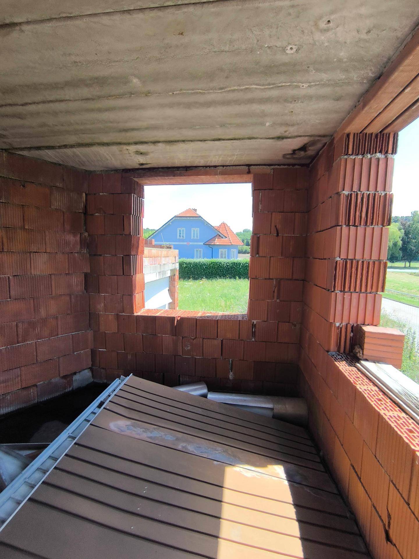 Unfertiger Innenraum mit Ziegelwänden und Fensteröffnung, die einen Blick ins Grüne bietet.