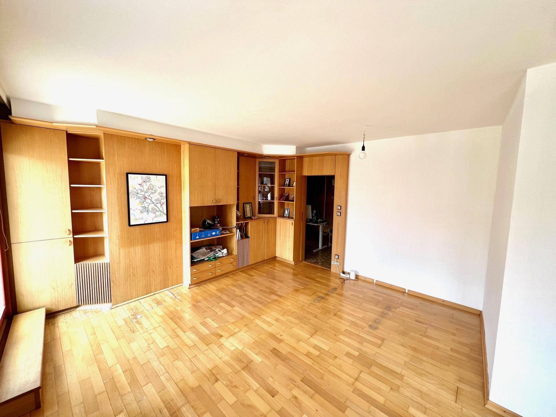 Helles Wohnzimmer mit Parkettboden und integrierten Holzschränken an der Wand, die viel Stauraum bieten.
