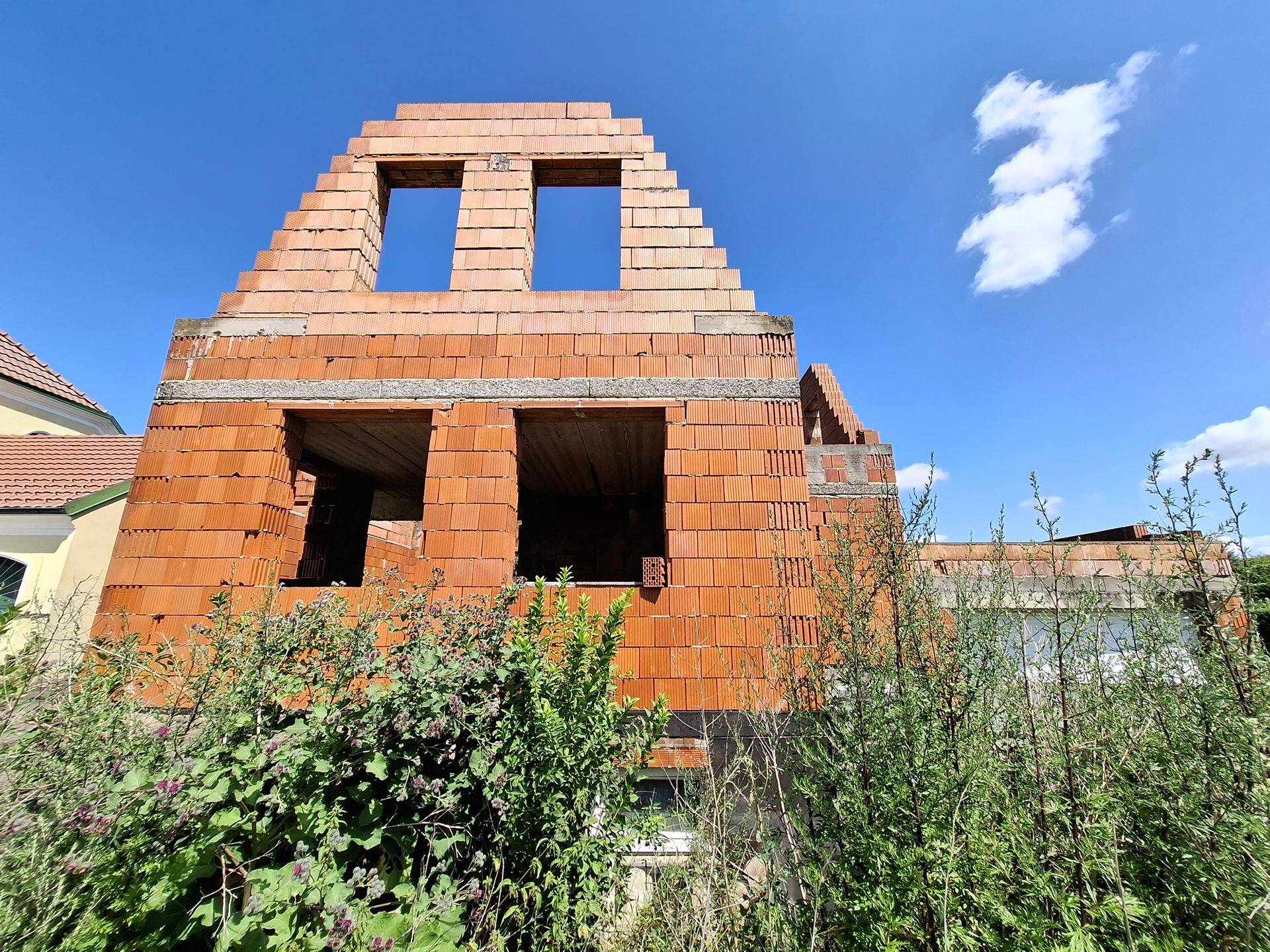 Seitenansicht des Rohbaus mit sichtbaren Ziegelwänden und Fensteröffnungen im Dachgeschossbereich.