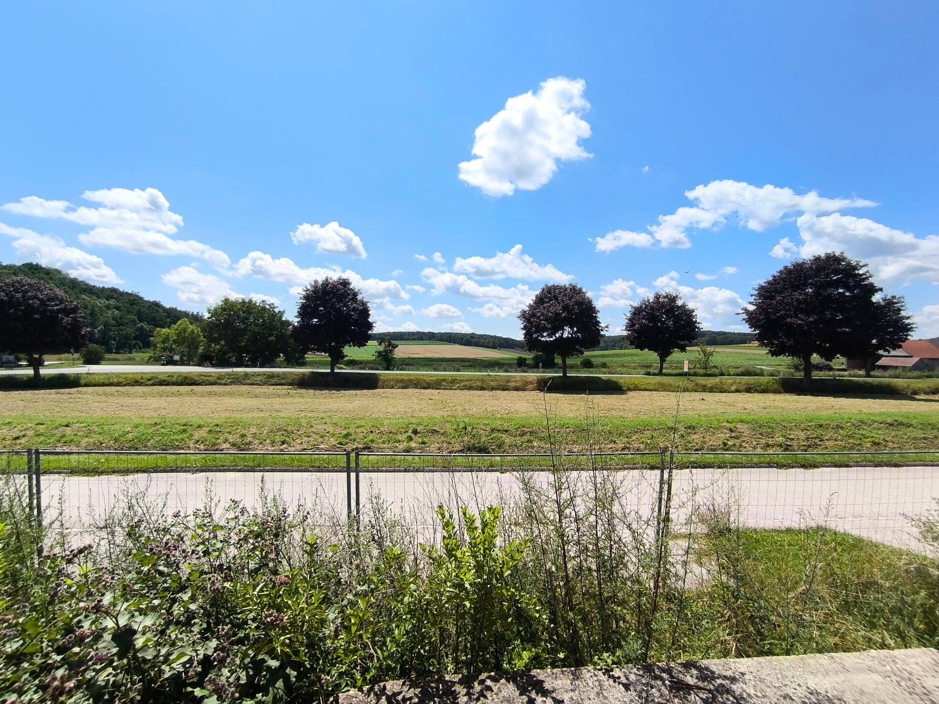 Weitläufige ländliche Landschaft mit Feldern, Bäumen und blauem Himmel, ideal für Naturliebhaber.