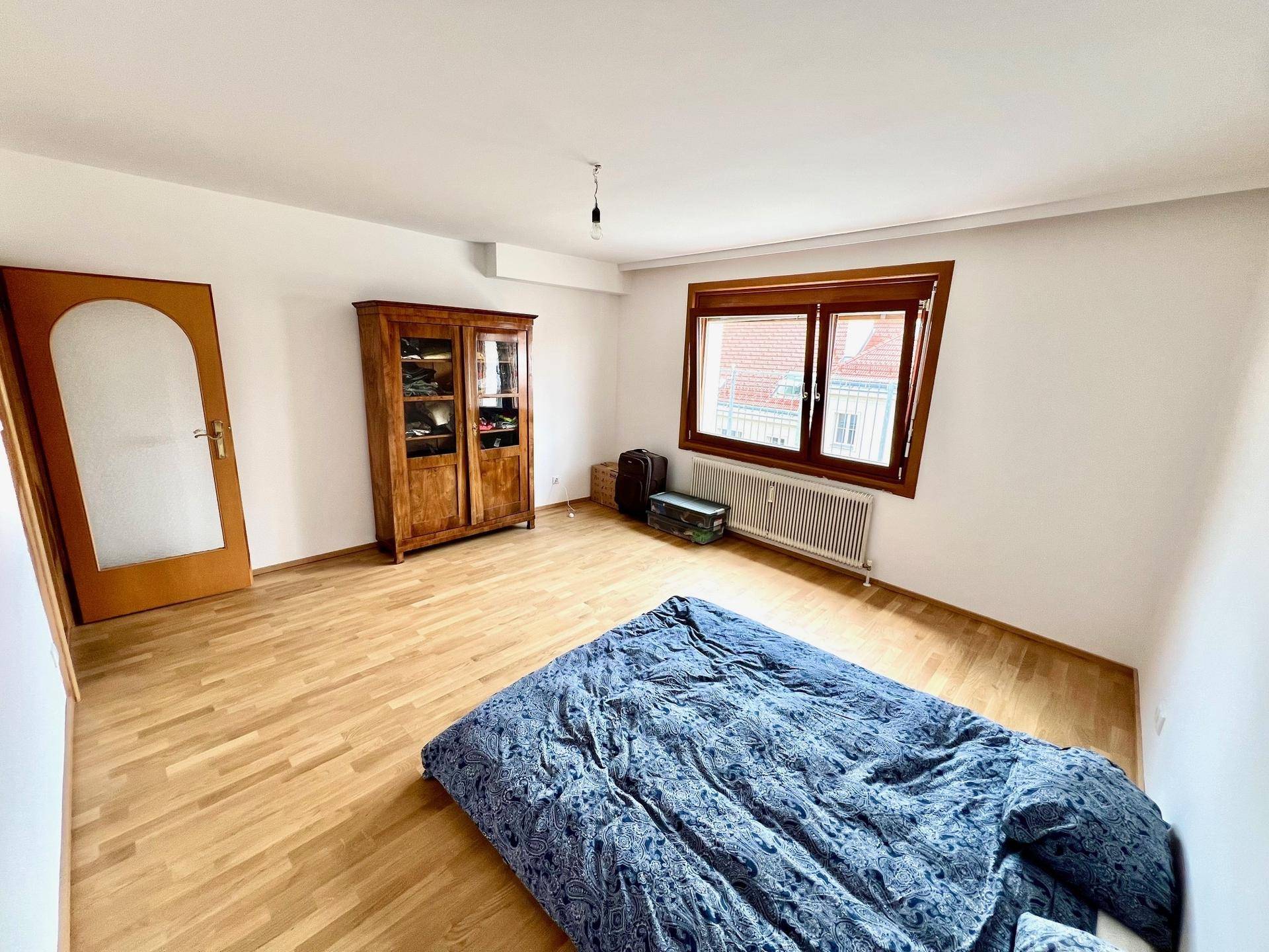 Helles Schlafzimmer mit Parkettboden und einem klassischen Holzschrank, der gut erhalten ist.