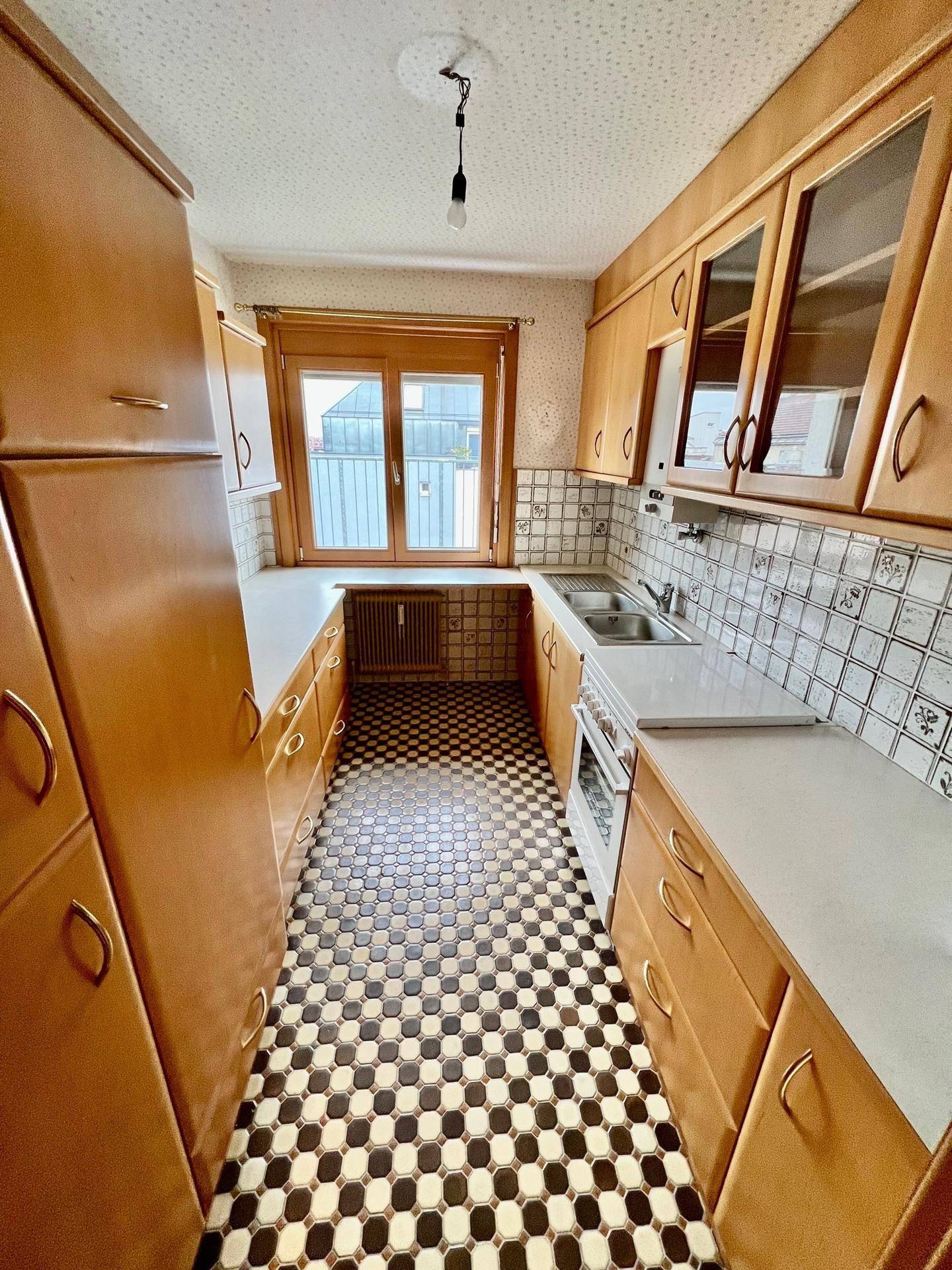 Küche im Vintage-Stil mit Holzschränken, kariertem Fliesenboden und einem Fenster, das Licht hereinlässt.