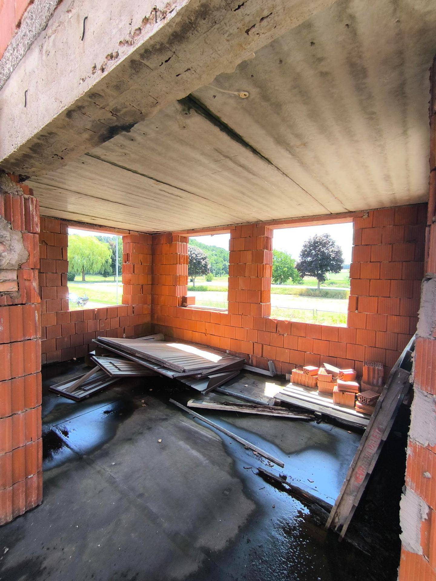 Rohbau-Innenraum mit mehreren Fensteröffnungen und Blick auf die umliegende Landschaft.