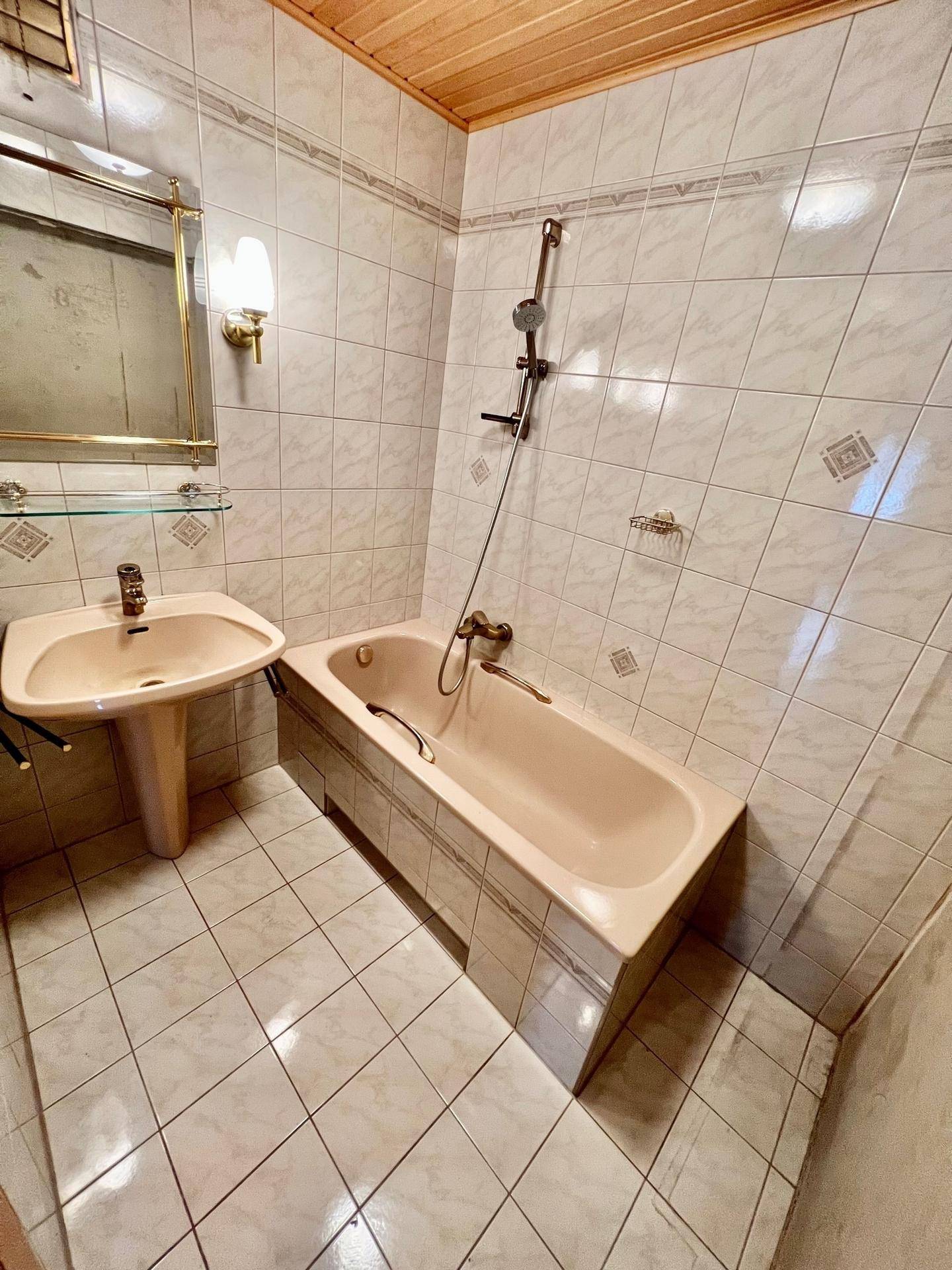 Badezimmer mit Badewanne, Waschbecken und gefliesten Wänden, sowie einer Holzdecke, die eine warme Atmosphäre schafft.
