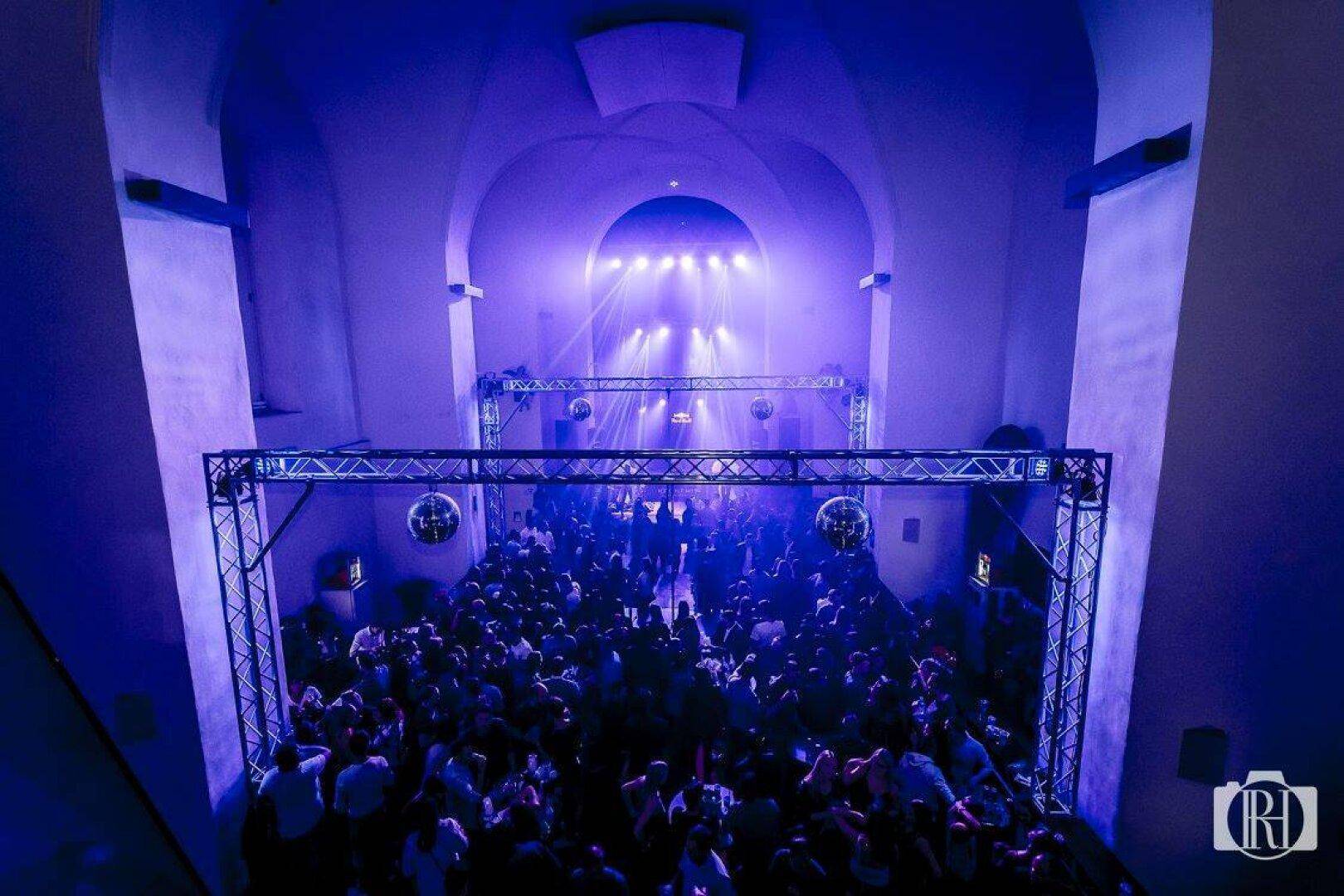 Großer Clubraum mit vielen tanzenden Menschen, Bühne und blauer Lichtshow, die eine energiegeladene Stimmung erzeugt.