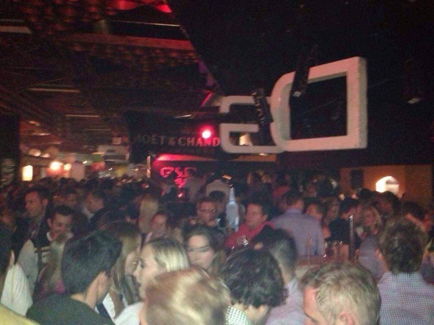Überfüllter Clubraum mit vielen Menschen, dunkler Atmosphäre und roter Beleuchtung, die eine intensive Stimmung schafft.