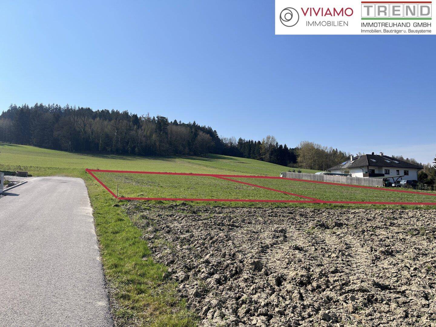 Weitläufiges Grundstück in ländlicher Umgebung mit grünen Feldern und Wald im Hintergrund.