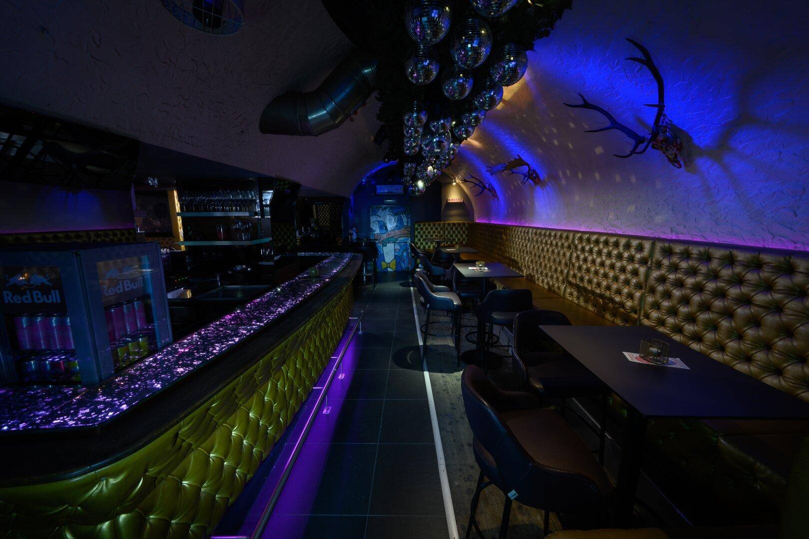 Langer Barbereich mit glitzernder Theke, gepolsterten Wänden und vielen Discokugeln an der Decke für eine festliche Stimmung.