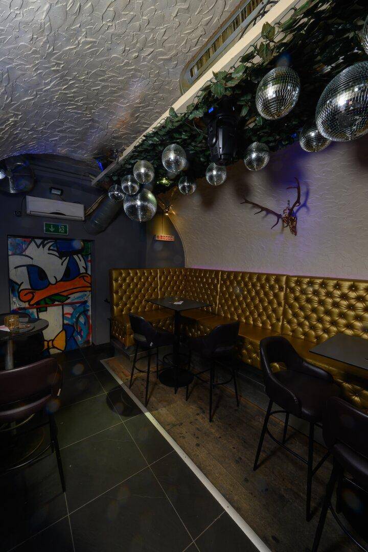 Gemütlicher Sitzbereich in einer Bar mit goldgepolsterten Bänken und vielen Discokugeln, die das Licht reflektieren.
