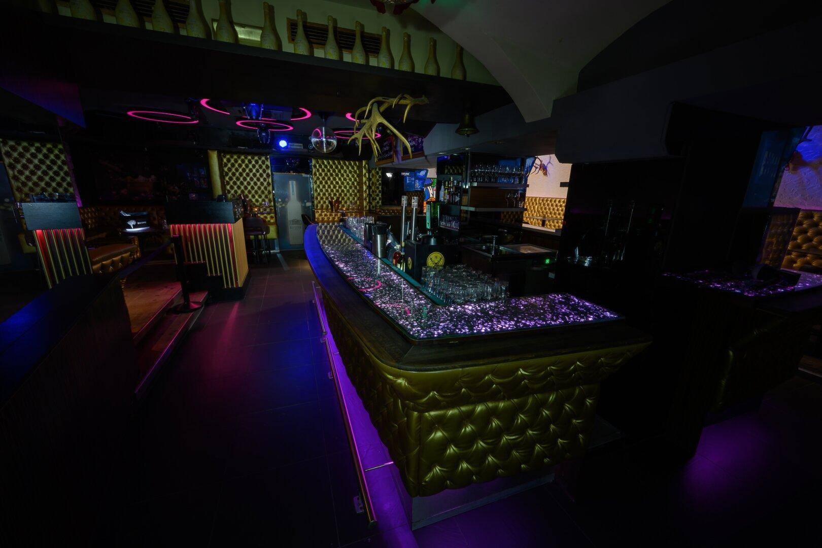 Bar mit glitzernder Theke, goldgepolsterten Sitzbereichen und dunkler, stimmungsvoller Beleuchtung für eine exklusive Atmosphäre.