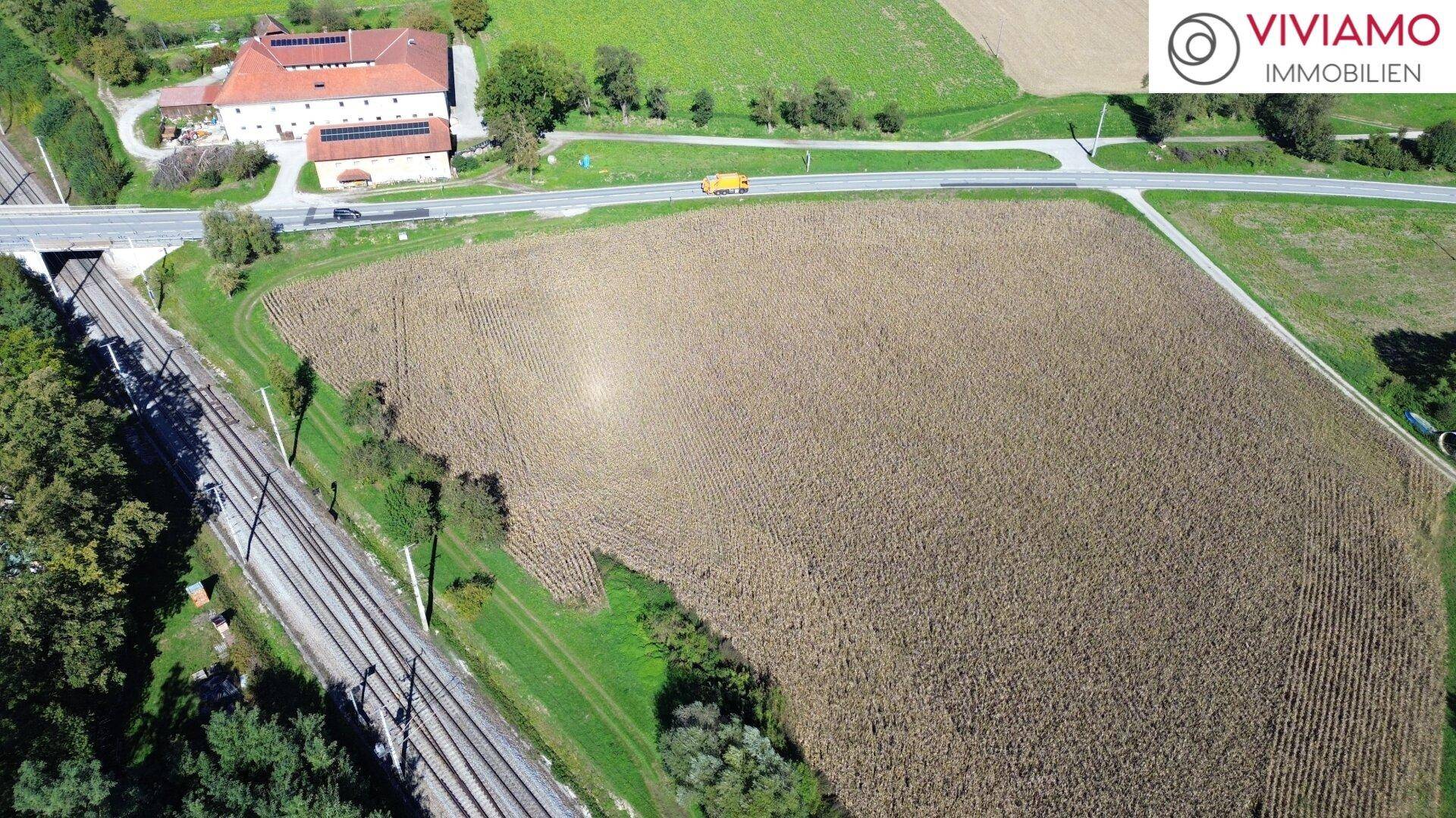 Luftbild eines Feldes neben Bahngleisen und einer Brücke, mit einem traditionellen Gebäude im Hintergrund.