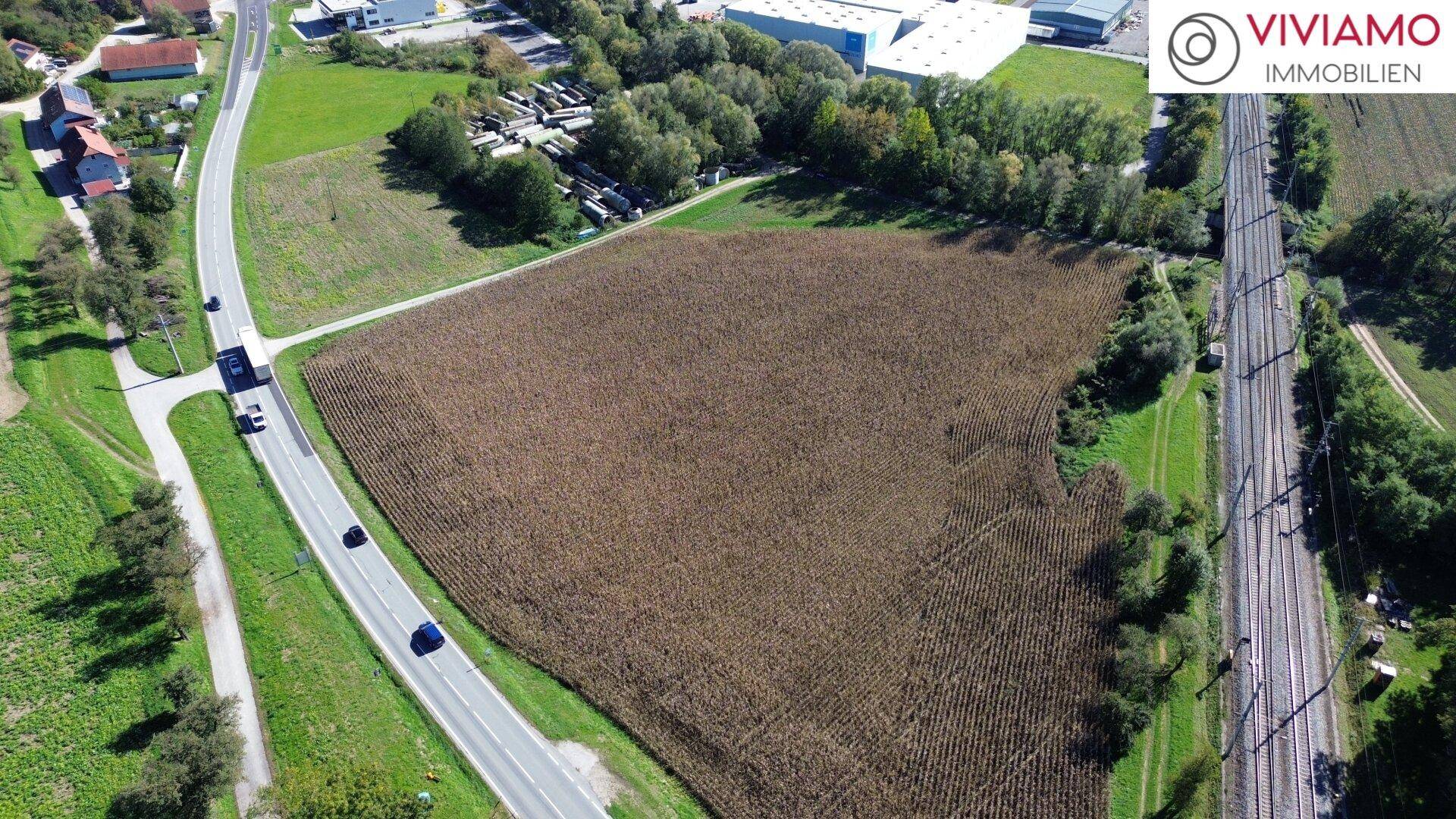 Luftaufnahme eines großen Feldes, umgeben von Straßen und Bahngleisen, mit Gebäuden in der Ferne.
